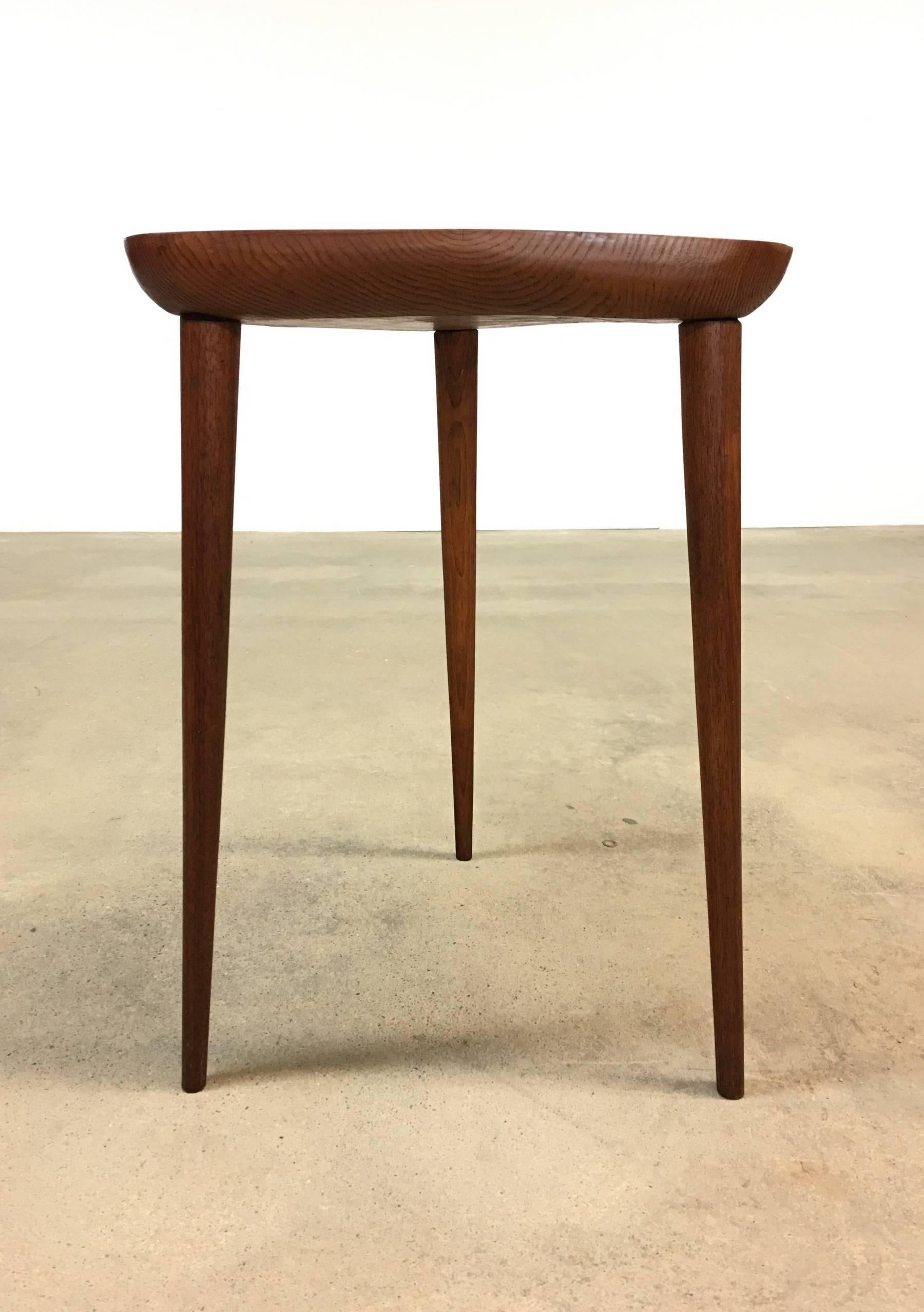 Tripod table in oak, teak and ebony, by Phillip Lloyd Powell, circa 1974. Table consists of a triangular shaped top, with chipped carved edge, and chip carved / hand-shaped teak legs that join the top with through-tenon construction, and are held in