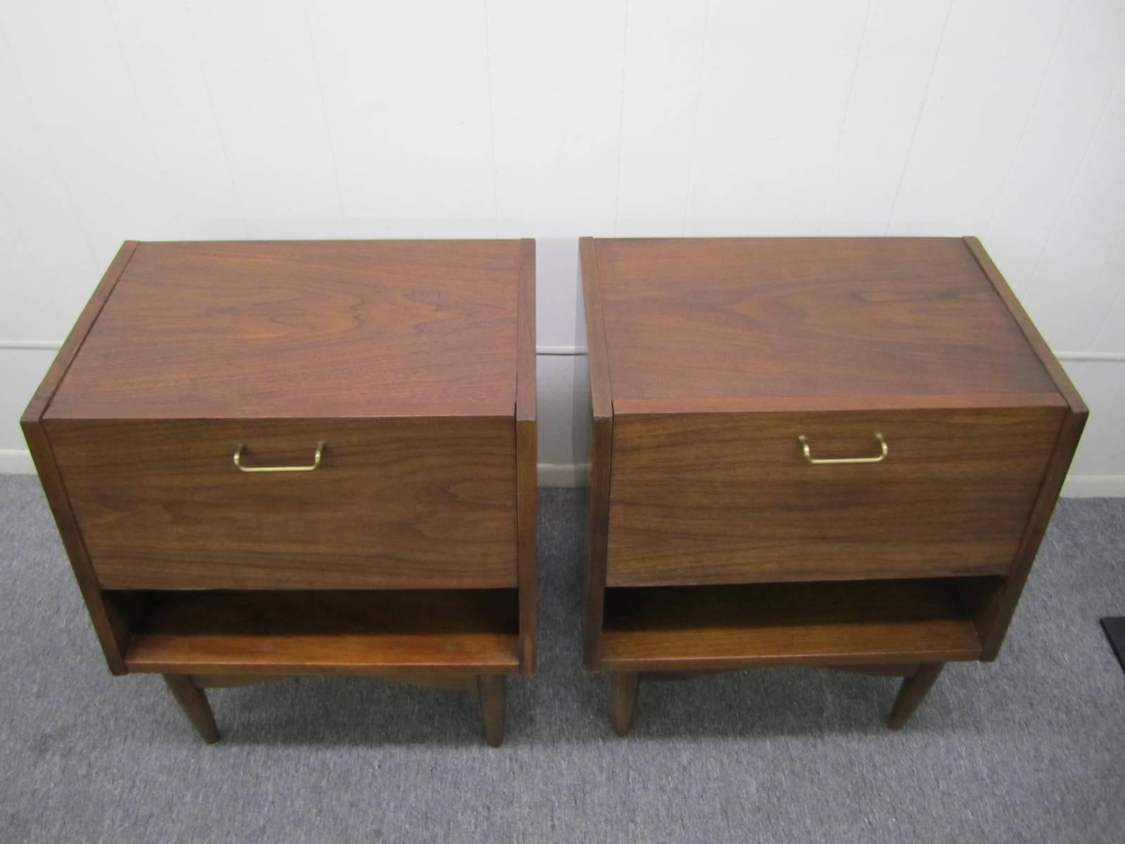 Great looking pair of American of Martinsville walnut nightstands. These stylish nightstands have a great flip down door opening to reveal a nice open space with on small drawer. The inside of the door has a durable Formica finish and works great