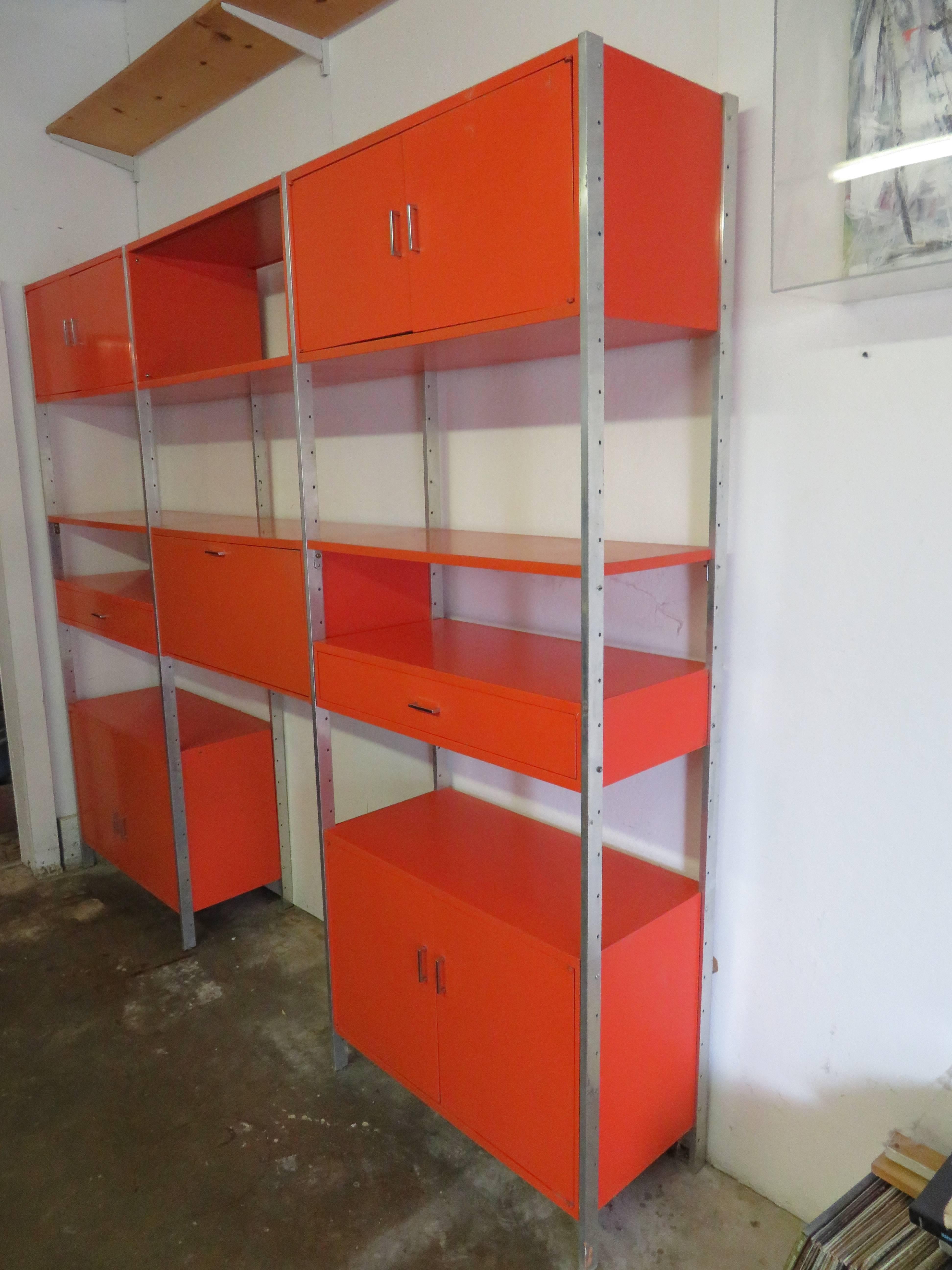 Unusual and rare orange lacquered three bay wall units by Founders. There are eight aluminum side rails, five large cabinets, two smaller drawer cabinets and two shelves. All retain their original orange lacquer in nice condition with light wear to