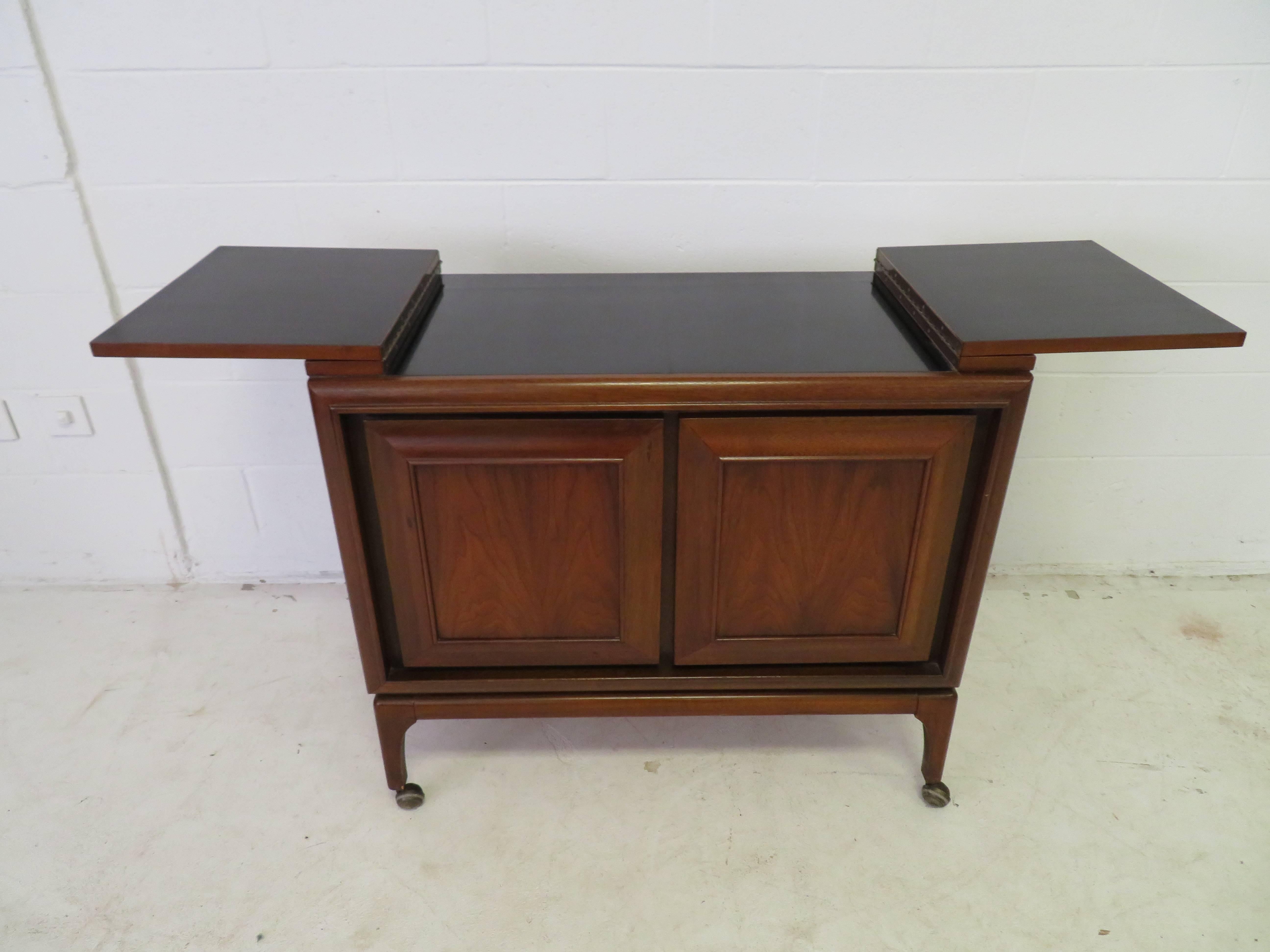 Handsome American Mid-Century Modern walnut rolling bar cart. The top flip open to reveal a nice black formica surface-great for mixing cocktails or used as an extra serving space during parties. The two doors open to reveal one divided drawer and