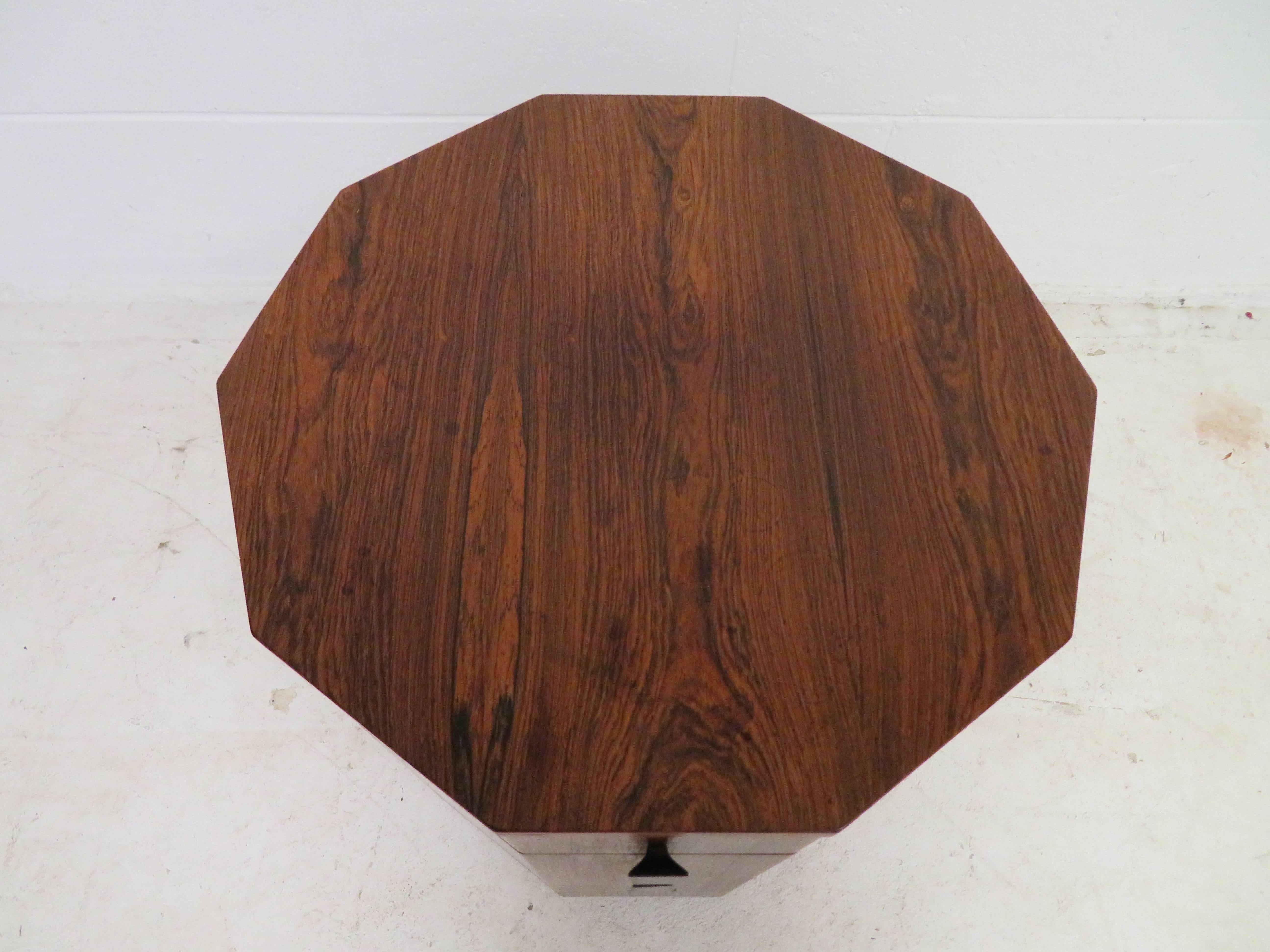 A ten-sided rosewood dry bar cabinet or lamp table with solid rosewood trapezoidal pulls. One drawer over door compartment and round wood plinth. Door incorporates two galleries for storing bottles. Designed and produced by Harvey Probber. American,