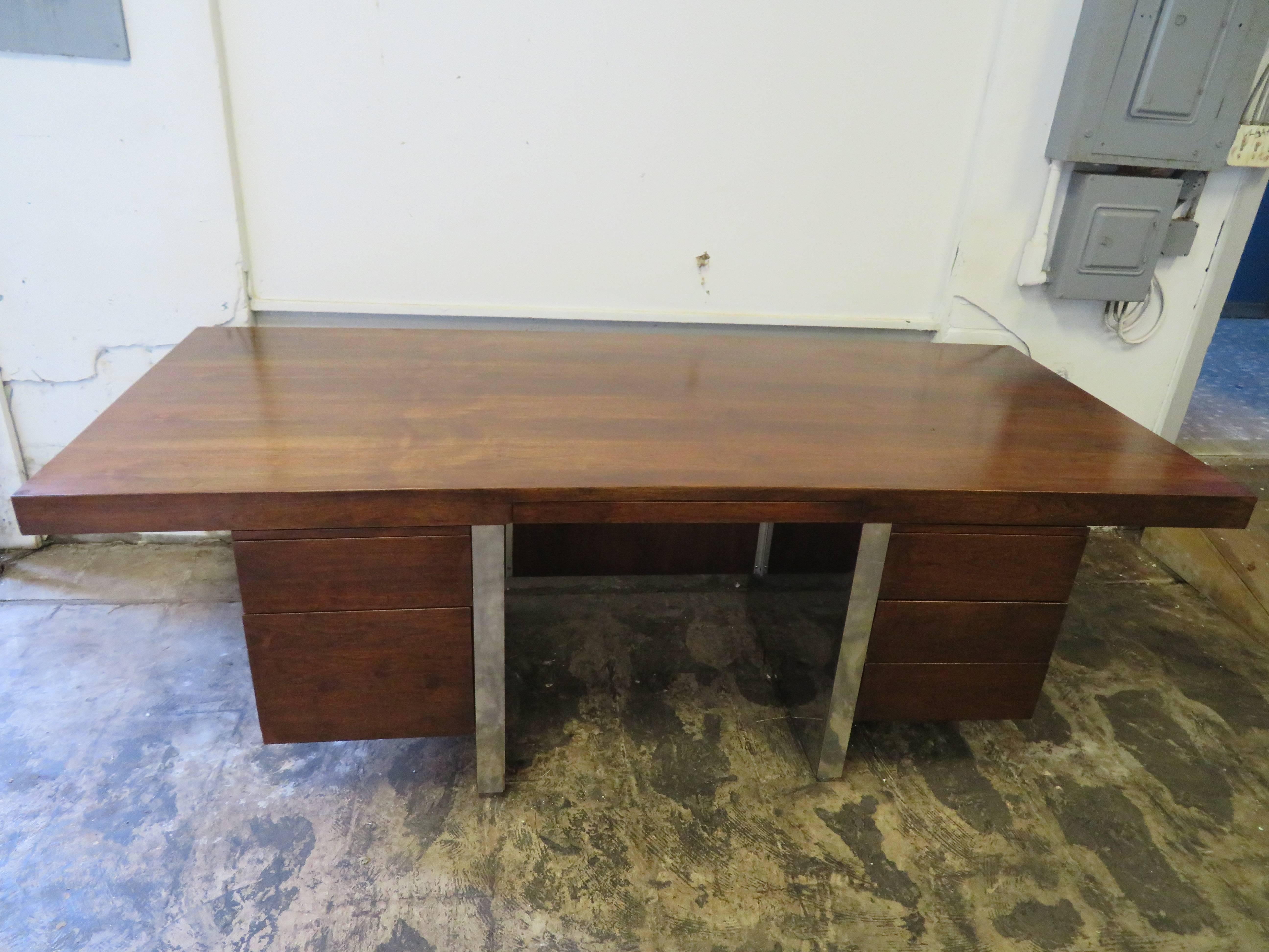 Large-scale Mid-Century Modern executive desk designed by Roger Sprunger for Dunbar. Gorgeous walnut with stainless steel double pedestal base. Four drawers including one file, two regular and central slender pencil drawer. Two pullout trays are
