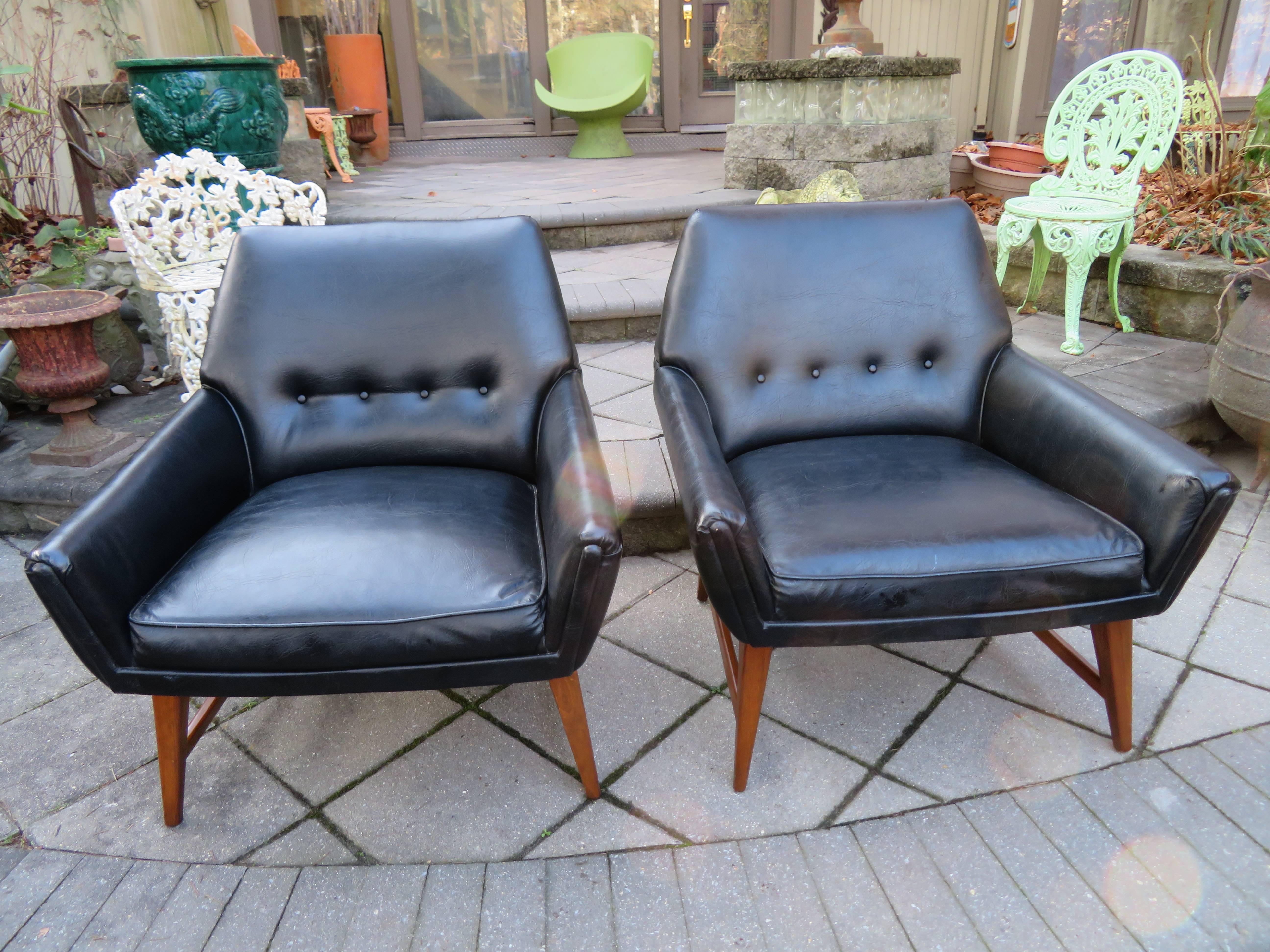 Handsome pair of Danish modern walnut base lounge chairs. We love the stylish wide low profile and sexy vibe these chair exude. Nice as is with their original faux black leather upholstery or reupholstered in something fresh and fun.