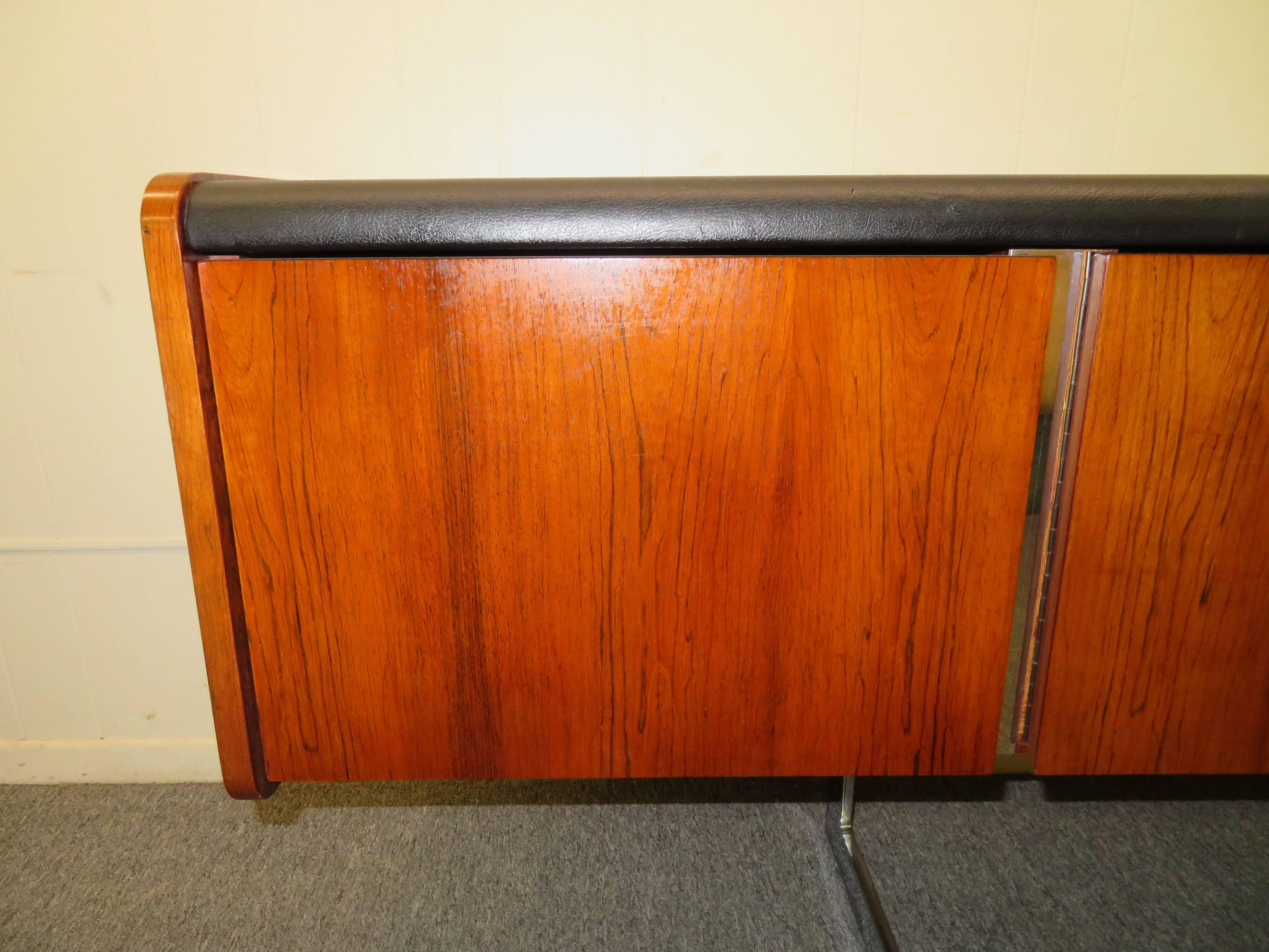 This Ste-Marie and Laurent sideboard has beautiful rosewood grain and a black faux leather top. This Mid-Century credenza floats on a modern chrome cantilever base and is finished on all sides. Left drawer holds hanging files and would be perfect