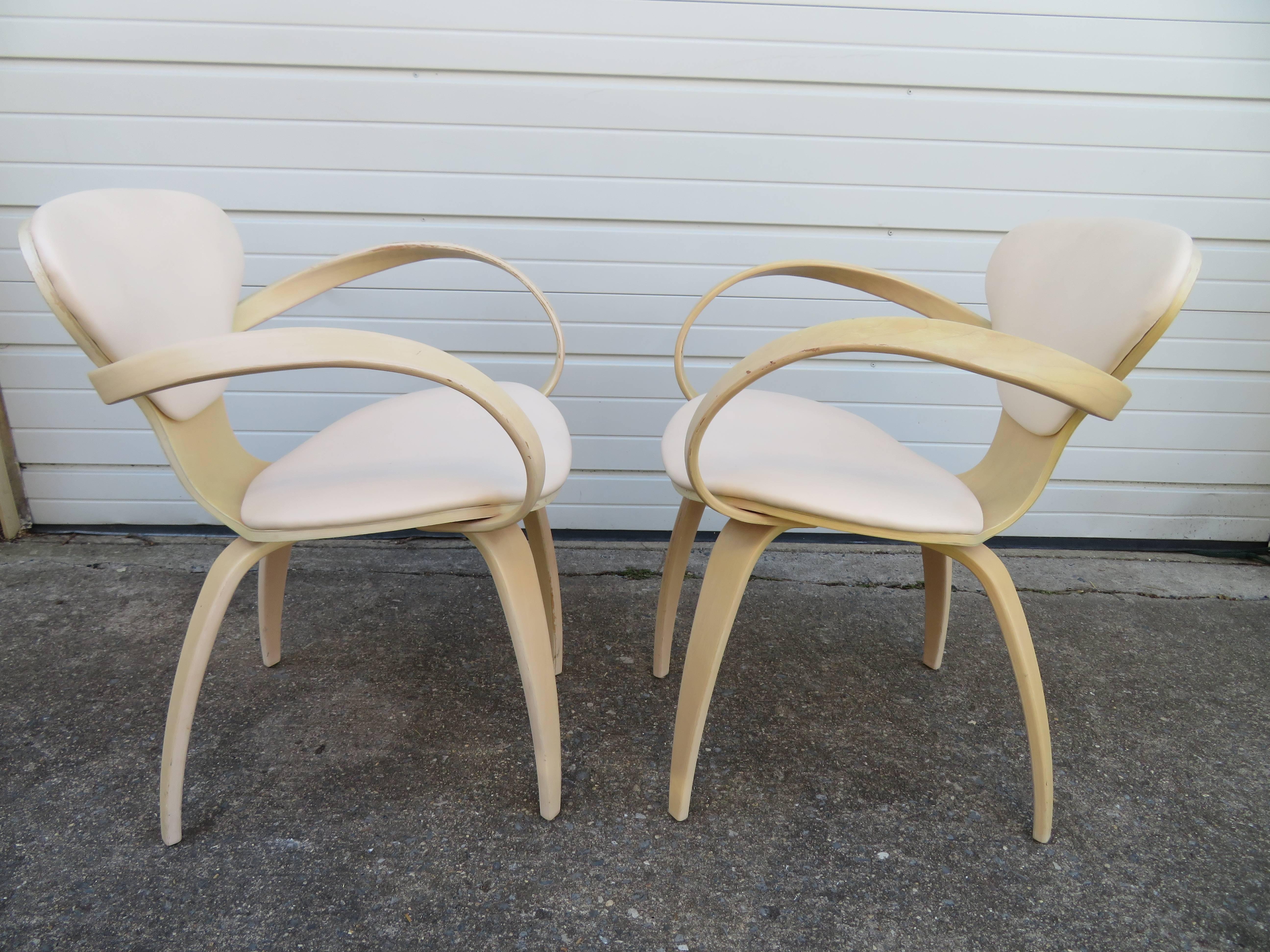 Lovely pair of labelled Norman Cherner Plycraft pretzel armchairs. This pair has a pickled white finish and bone colored faux leather in nice vintage condition.