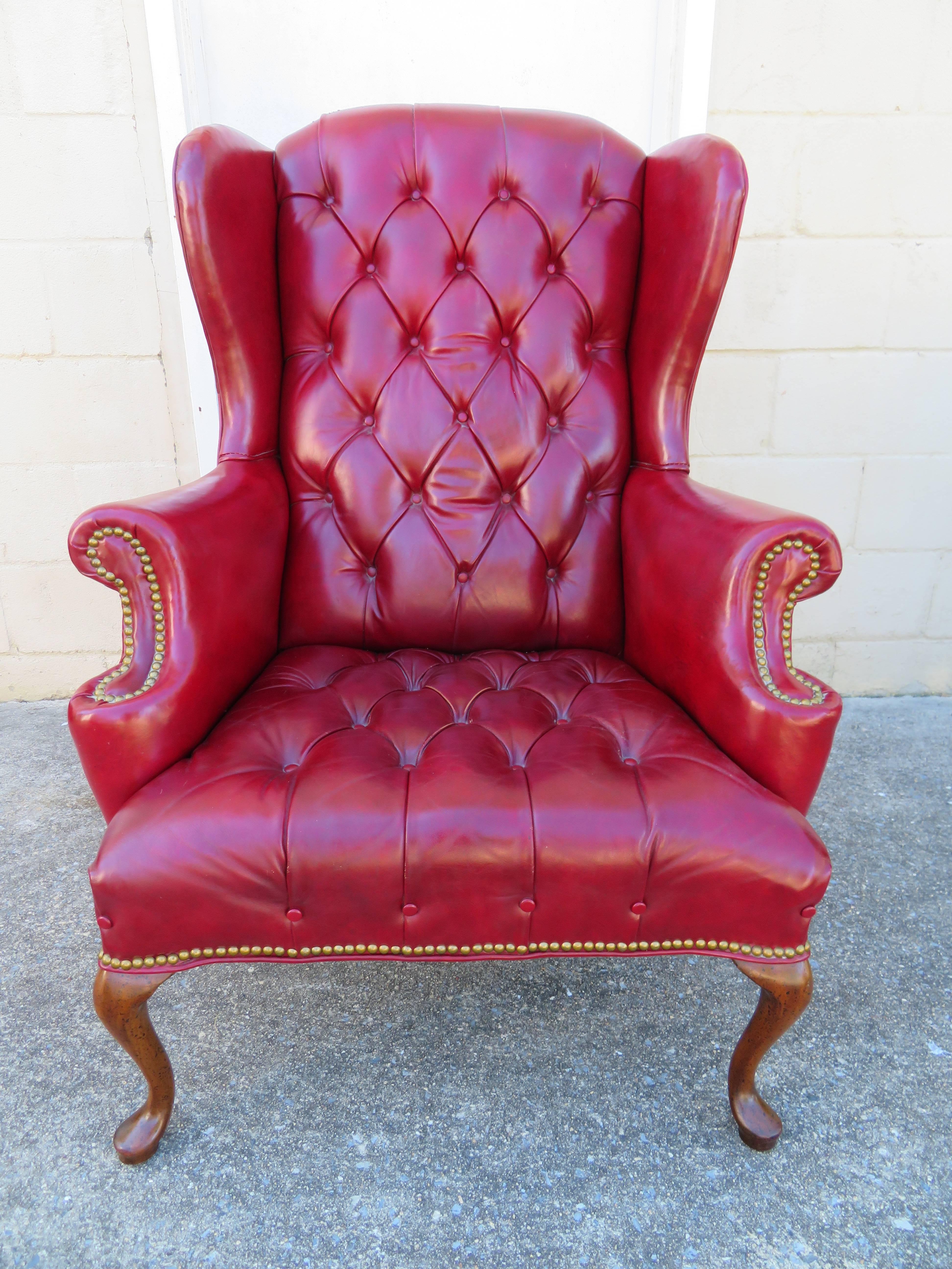 Handsome red leather tufted Chesterfield wingback chair with matching ottoman. This stunning set has great vintage appeal with slightly worn red leather and brass studded arms. The chair measures 44