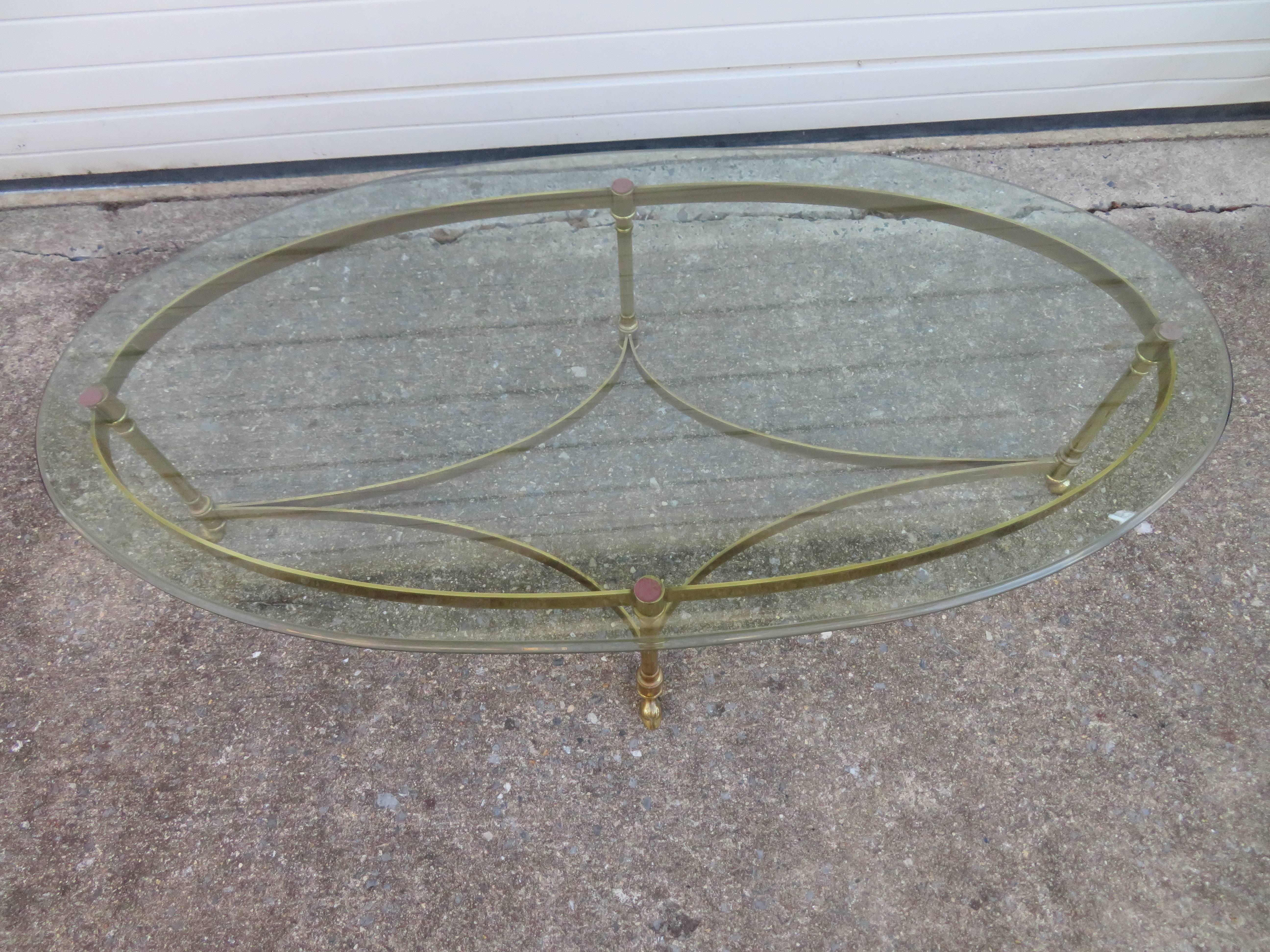 A classic brass and glass cocktail table by Labarge with oval glass top and iconic hoof footed brass base. We love the lightly patinated brass finish.