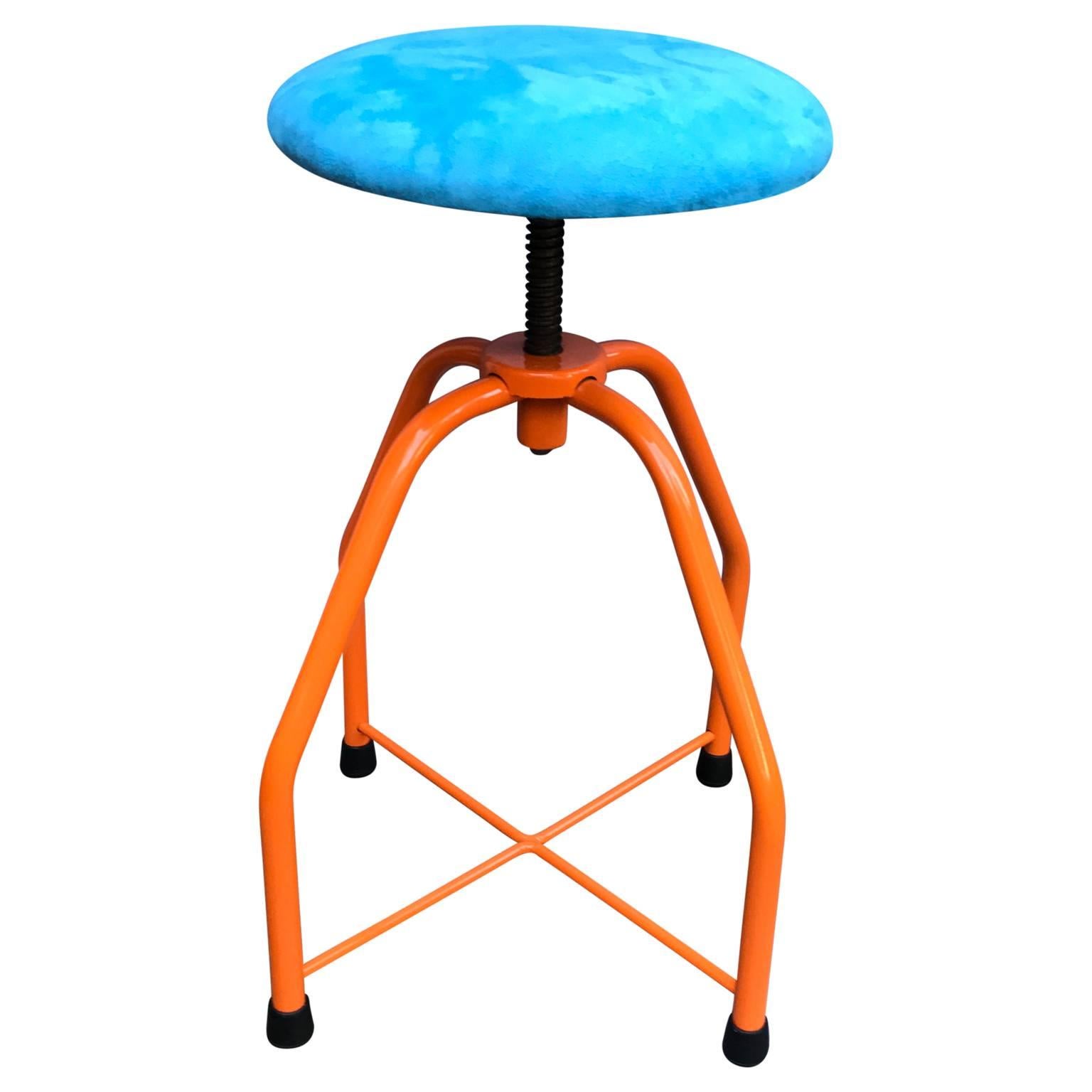 Bright orange Industrial era stool with blue faux suede fabric seat. This fun and bright stool has a seat that adjusts for height. Bold and mighty, this fun piece will be a great accent in a kitchen, mudroom or anywhere you want an eclectic stool.