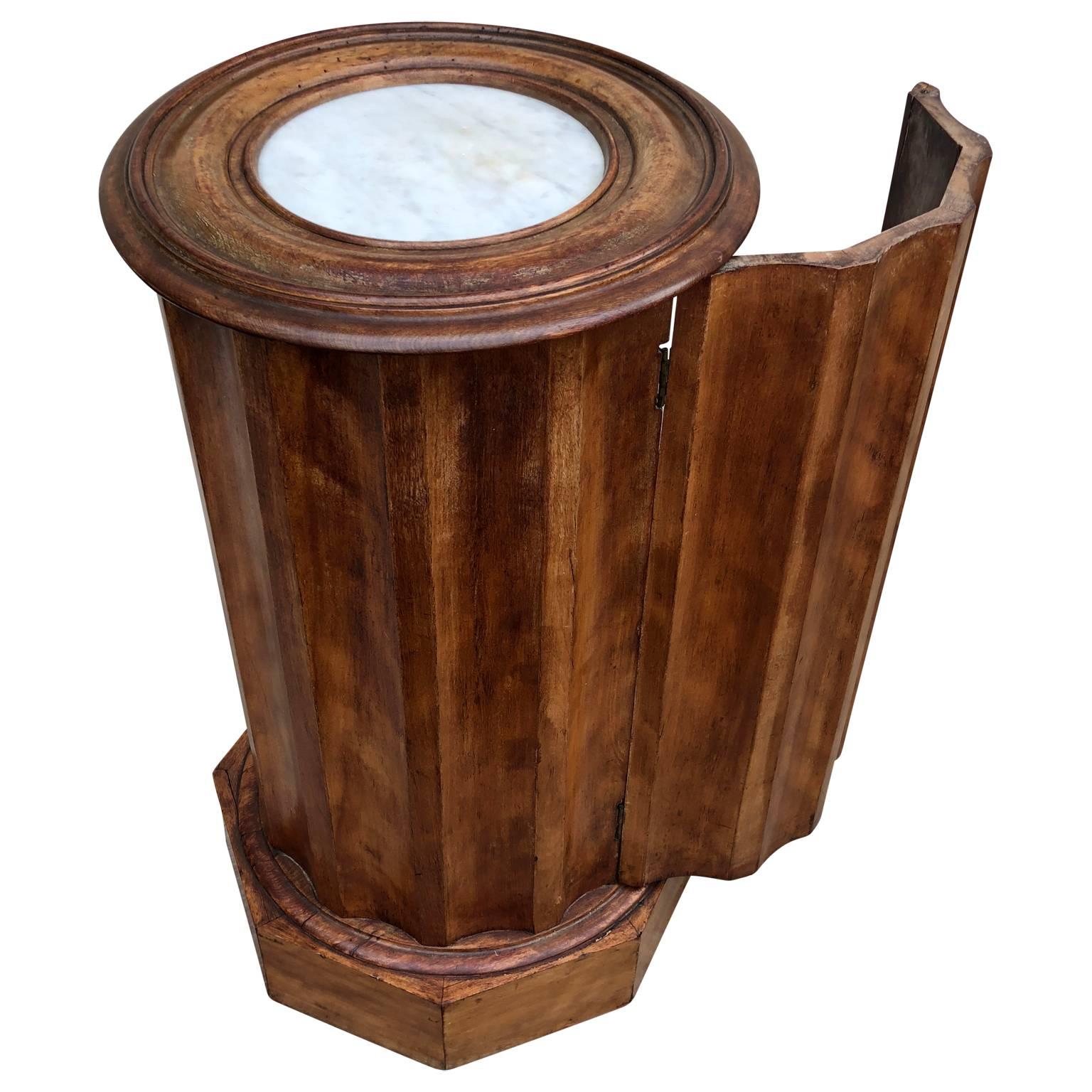 French 19th century Neo-classical style fluted wood and marble-top pedestal.
This wooden pedestal has two shelves behind a hidden door. The circular marble inlay on top makes the piece especially eye catching. It will serve as a plant stand or as a