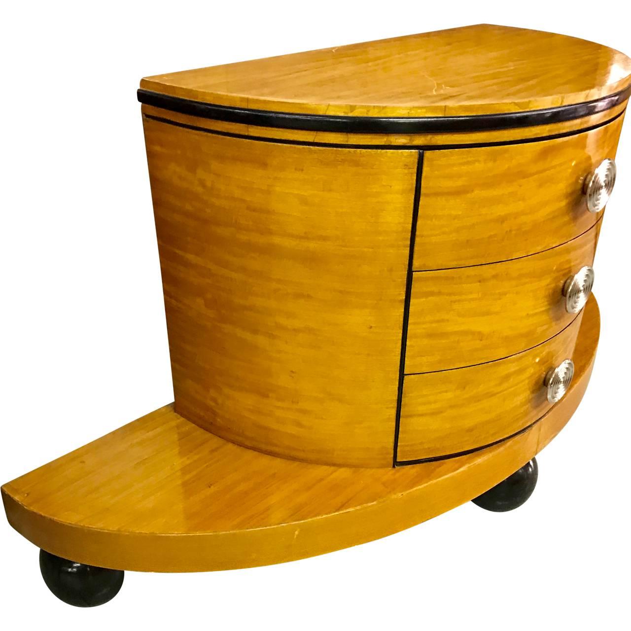 Elegante cómoda moderna de tres cajones sobre una amplia base demiluna. La base se apoya en tres bolas de madera pintadas de negro a modo de patas. Los herrajes cromados son 100% originales.
