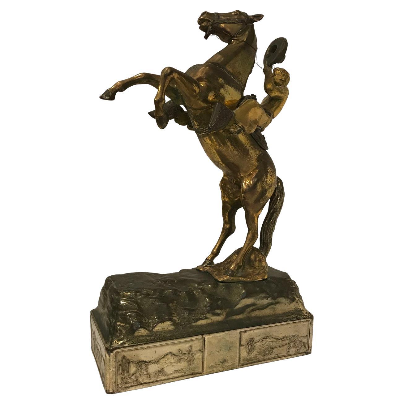 Escultura de latón dorado sobre peana, que representa a un vaquero celebrando sobre un caballo salvaje con gran pátina.