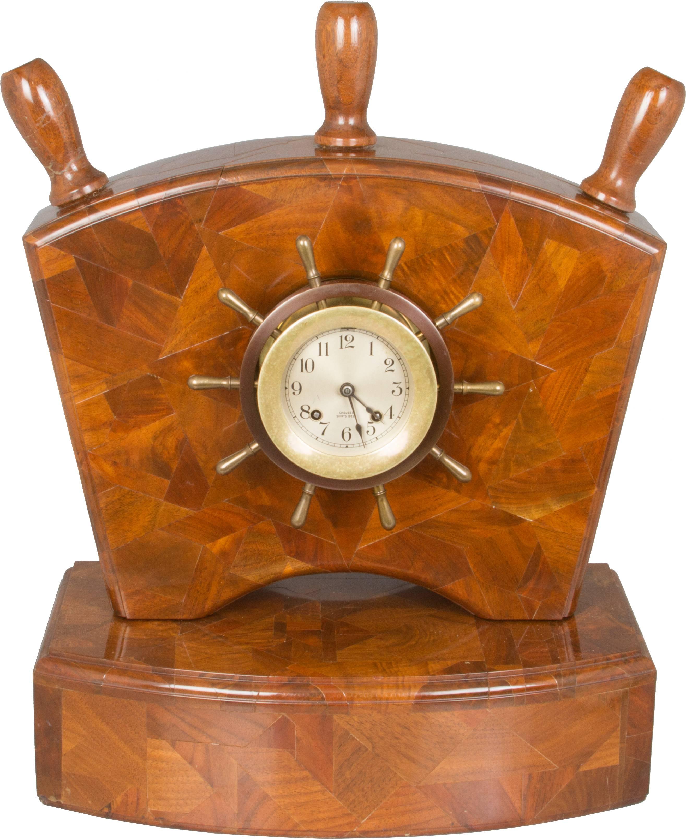 This is a fabulous piece! The clock is in the shape of a yacht's wheel and is mounted into a wooden parquetry holder, the design is also mimicking the elements of a ships wheel.