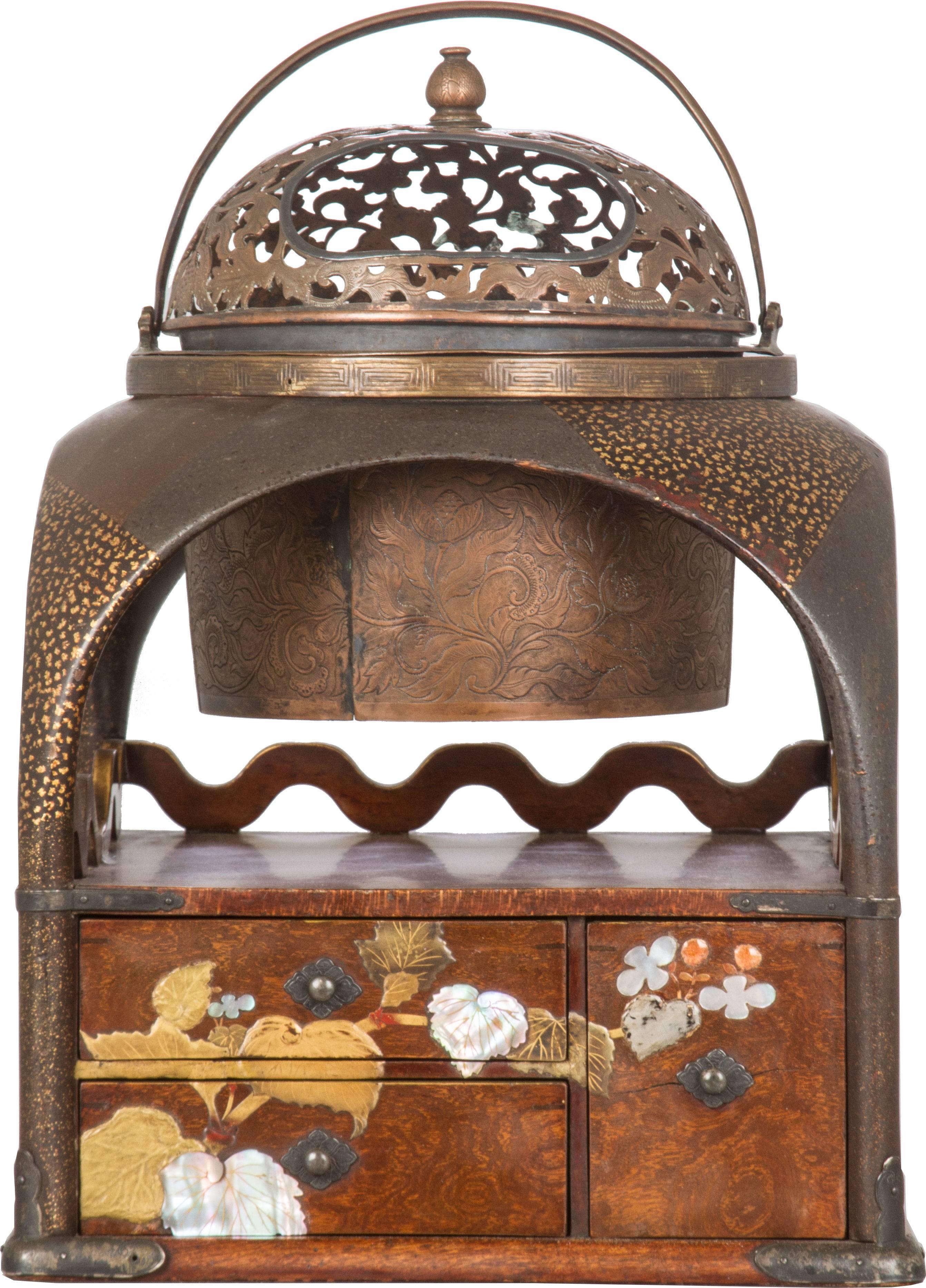 This is a beautifully crafted tabako-bon smoking box having beautiful applied mother-of-pearl flowers and subtle gold on black enamelling. The bronze brazier has open floral detailing on the top and raised detailing on the sides.