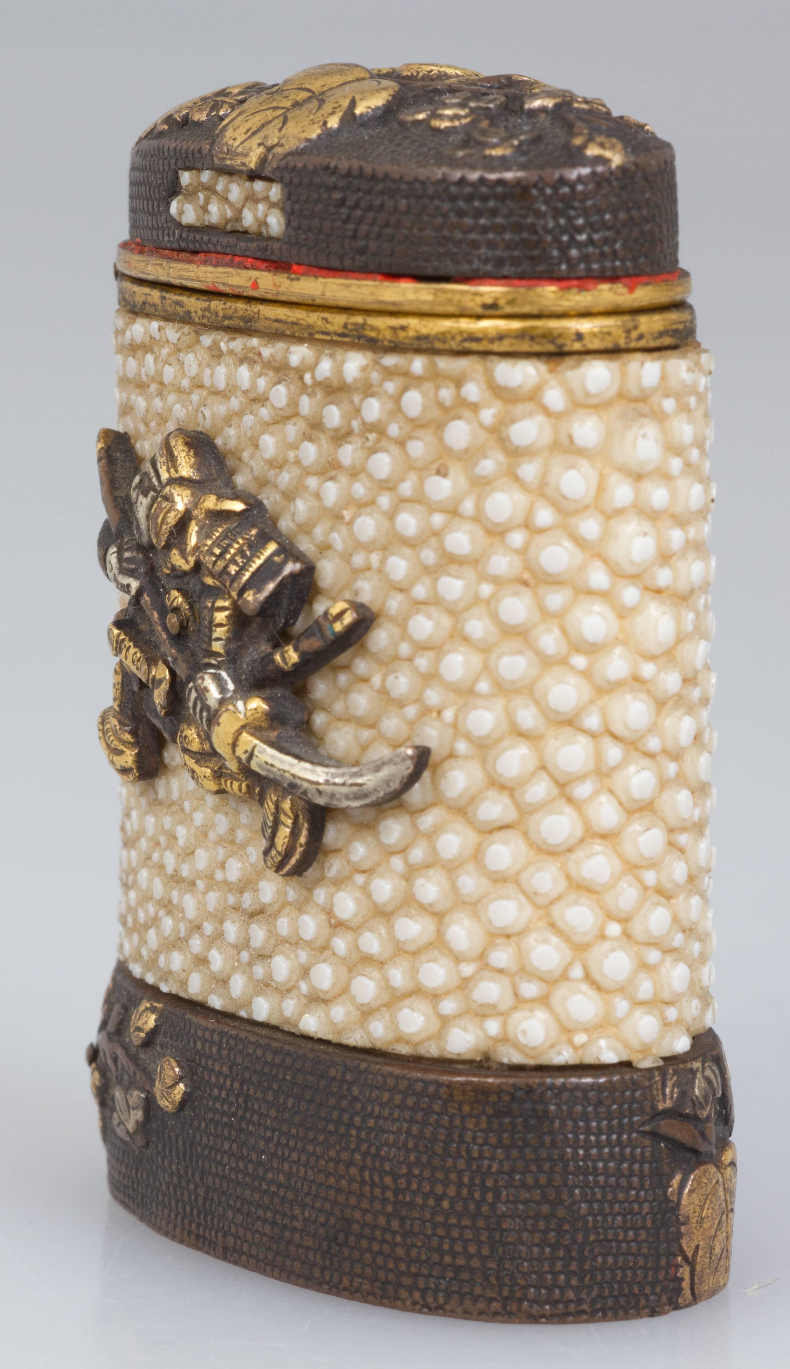 This is an unusual match safe, covered in shagreen with a samurai warrior applied to the body. Leaves and flowers decorate the hinged cover and bottom band. The striker is on the bottom.