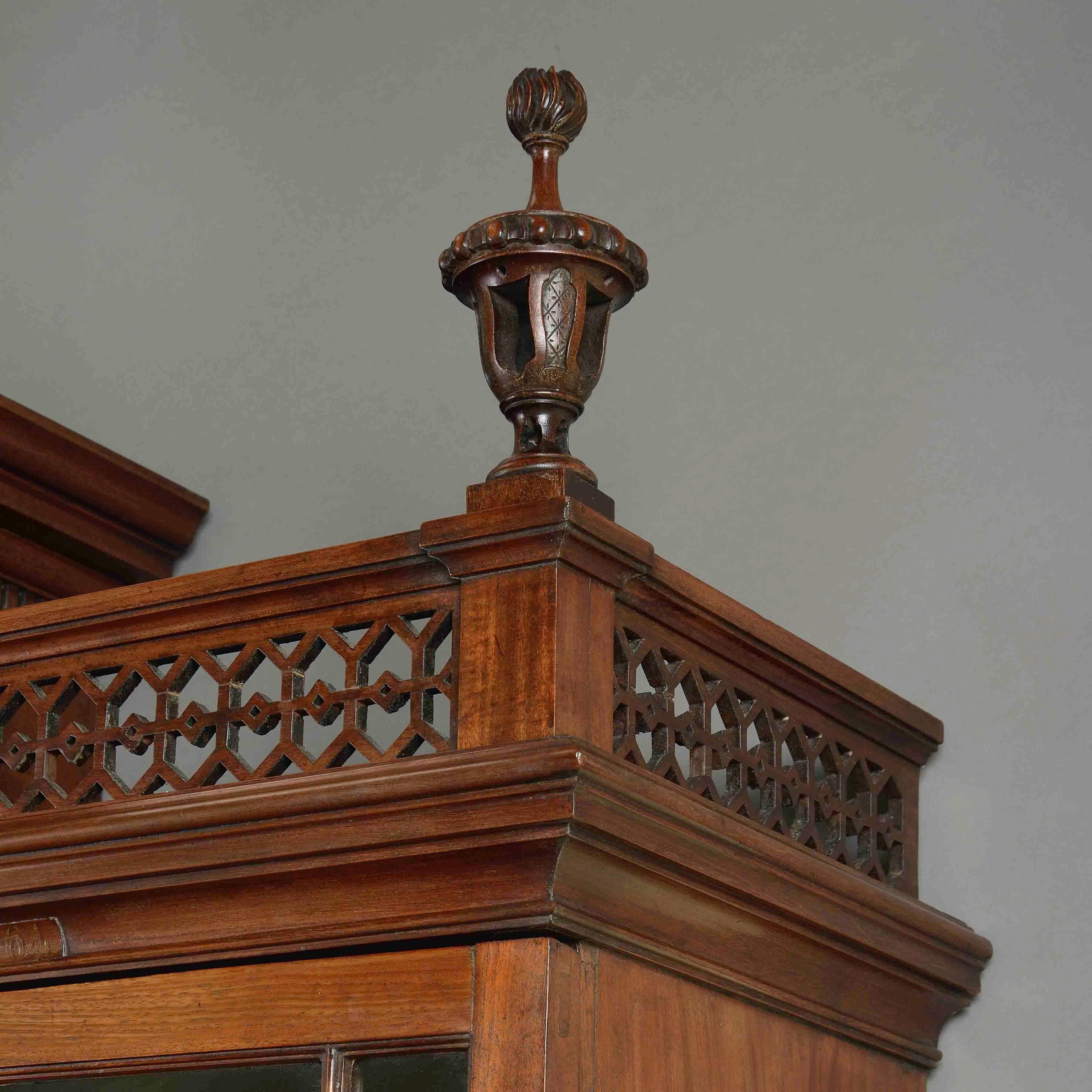 A fine George II mahogany breakfront bookcase in the manner of Thomas Chippendale, circa 1760.

The stepped top with broken pediment flanked by fret-pierced galleries, surmounted by three carved and pierced urn finials (two original, one replaced)
