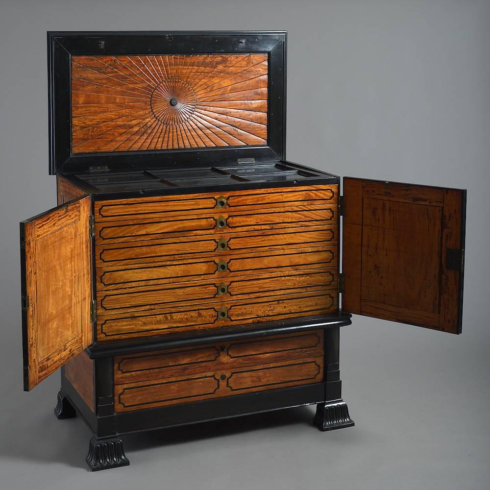 An unusual Anglo-Indian satinwood and ebony collector’s cabinet, circa 1830.

South Indian or Ceylon. The hinged top enclosing a display draw above seven further draws.
  