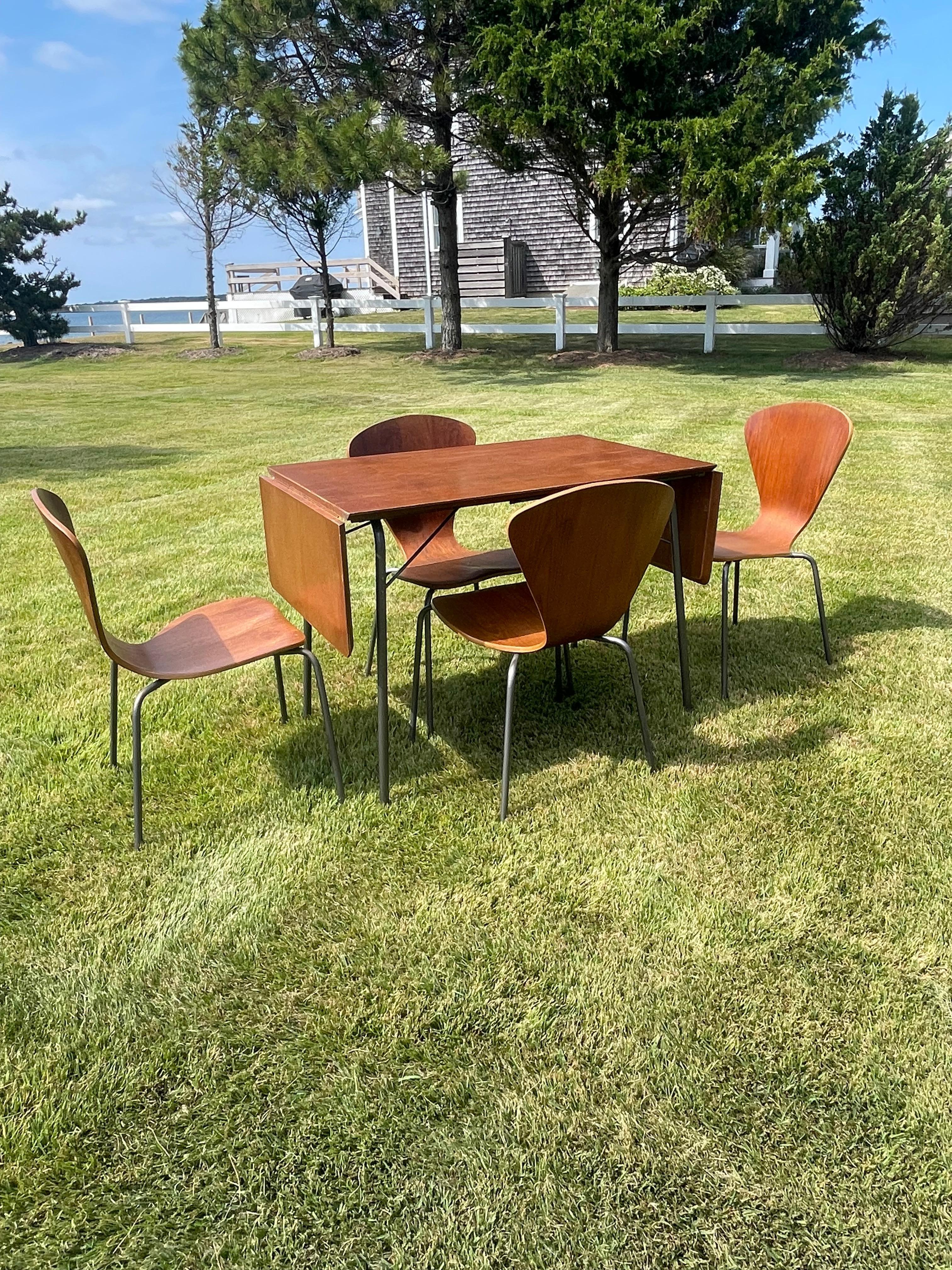 Mediados de siglo  El juego moderno danés no tiene marca y es del estilo del juego de camping de Arne Jacobsen de los años 60. La mesa y las sillas tienen patas de tubo hueco de acero. La mesa es plegable y extensible por ambos lados. La mesa mide
