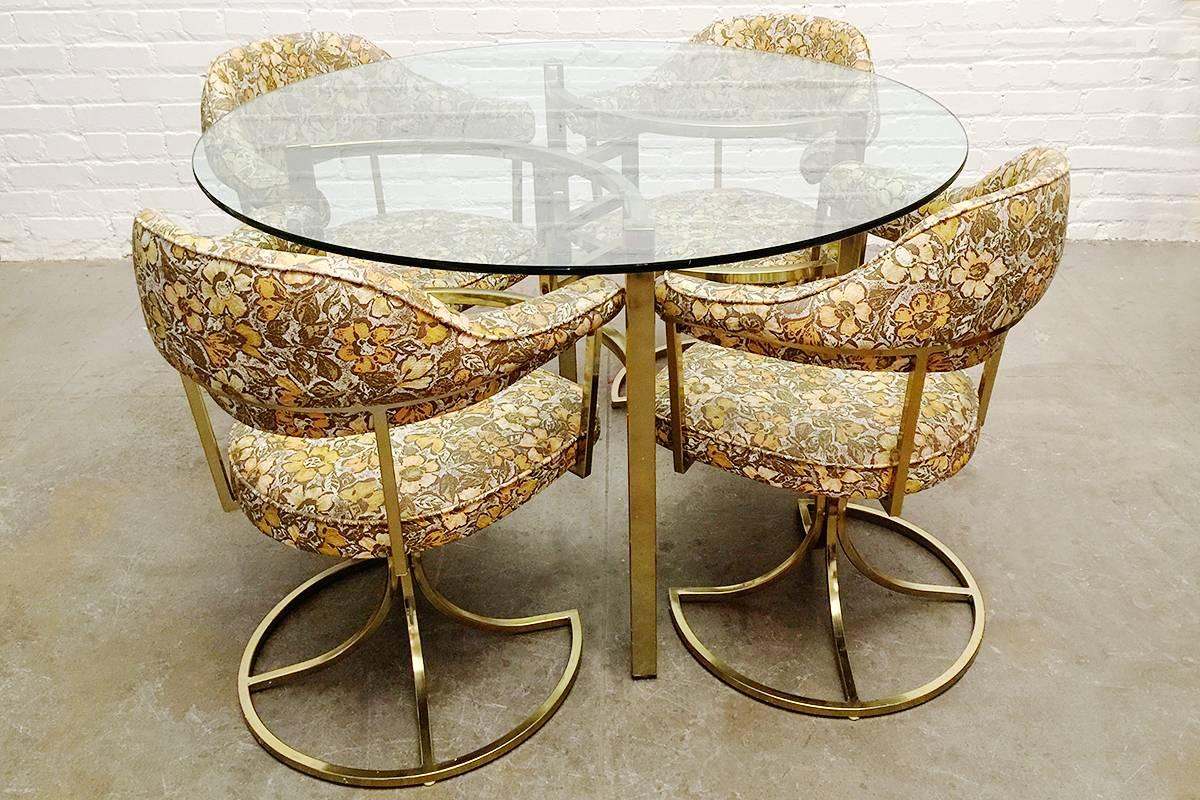 Awesome glass and brass dinette table with four matching chairs. Minimal square tube design with great curves in center of table base. Super 1970s swivel chair base design with original floral vinyl. (New upholstery available).

Table: 46