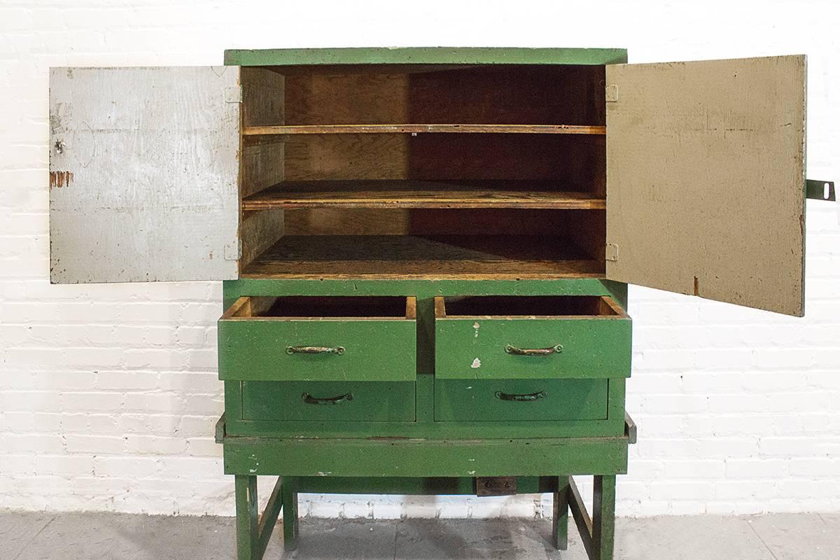 Fantastic handmade machinist's cabinet from the 1920s. Cabinet features two large doors and four drawers and is removable from stand. Original distressed olive paint. Perfect for the workshop or retail merchandising.

Measures: 42