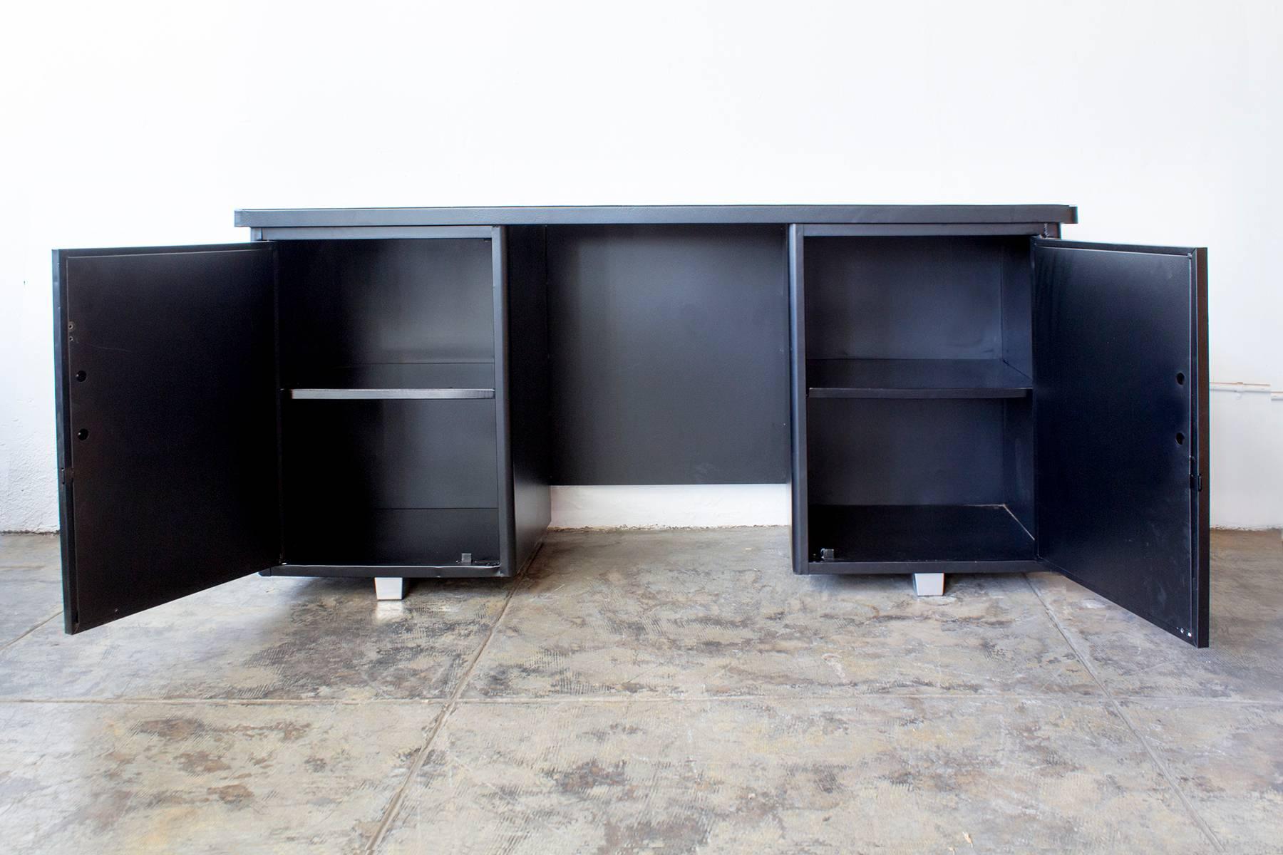 Our 1960s knee-space tanker credenza is a console table with the added functionality of a slim desk. This Classic mad men era piece offers ample storage, including two multi-shelf cabinets. We restored this piece in a beautiful semi-gloss black