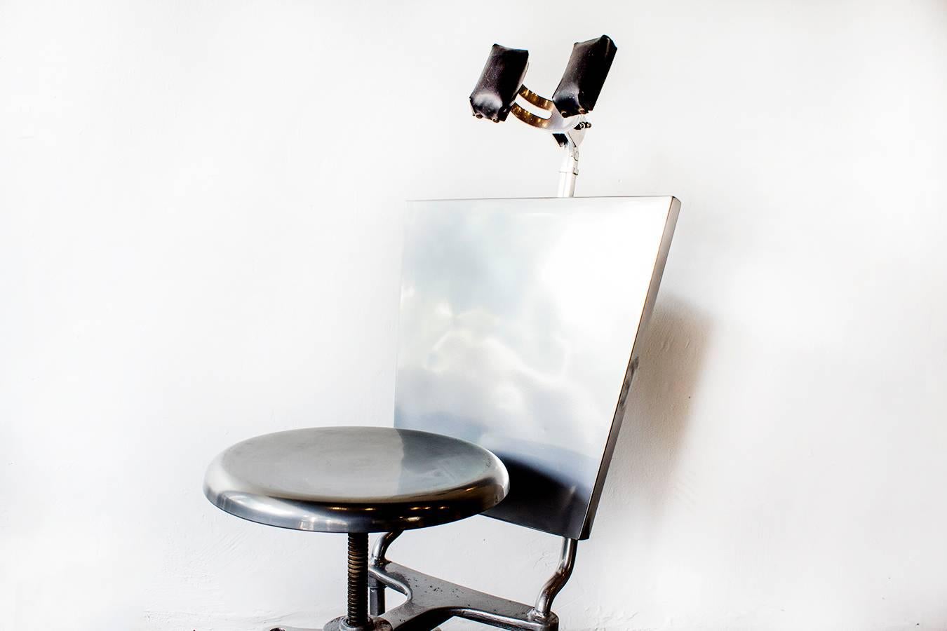 A most unusual industrial era medical exam chair, circa 1930. We refinished this streamlined steel piece in metallic silver with a newly reupholstered leather headrest. Features adjustable seat and headrest. In excellent refinished condition.