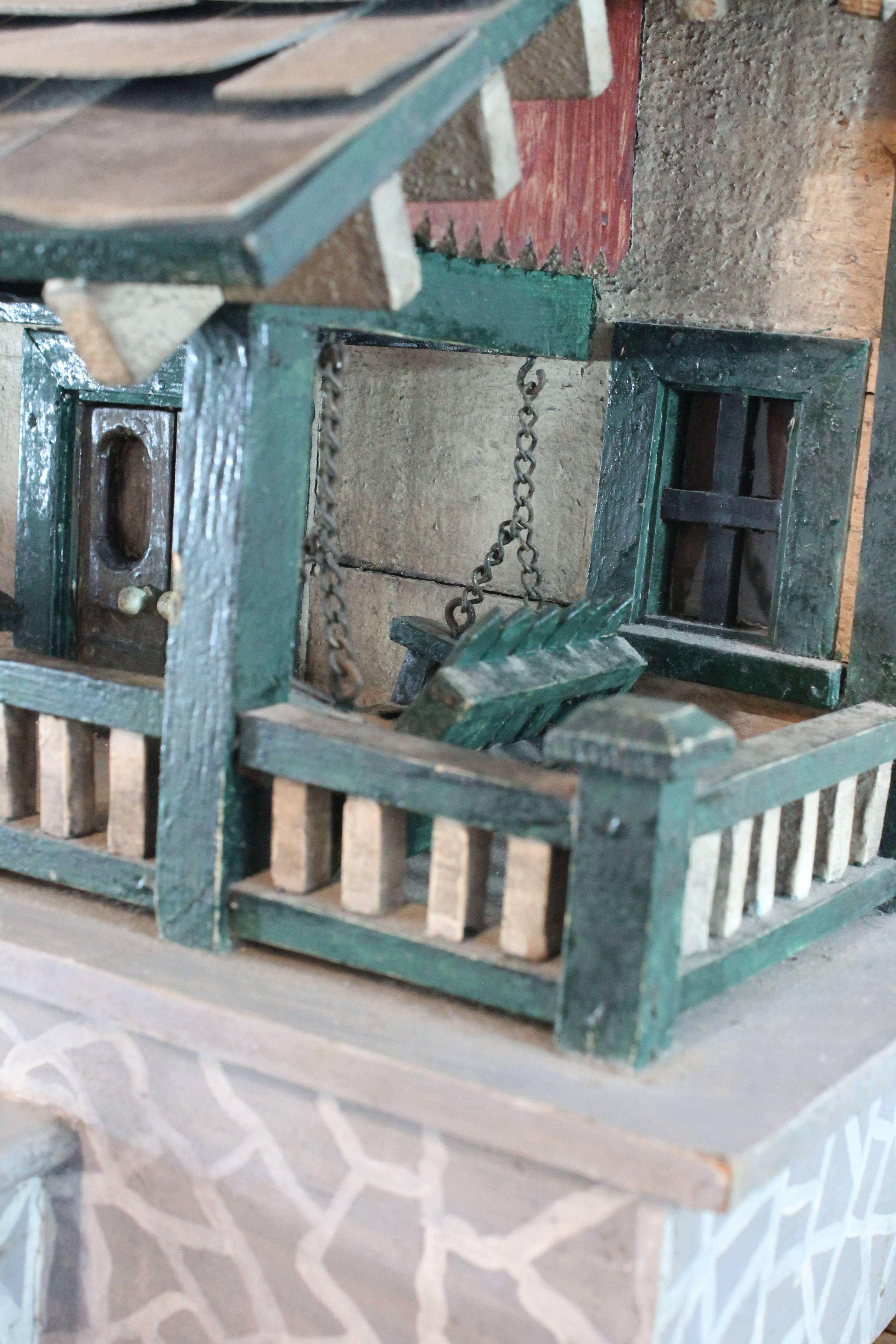 Exceptional Folk Art handmade architectural model from the early 20th century.
The front porch is complete with a swing. Great hand-painted faux stone fronted deck and stairs. Wonderful simple architectural details from the front doors to the