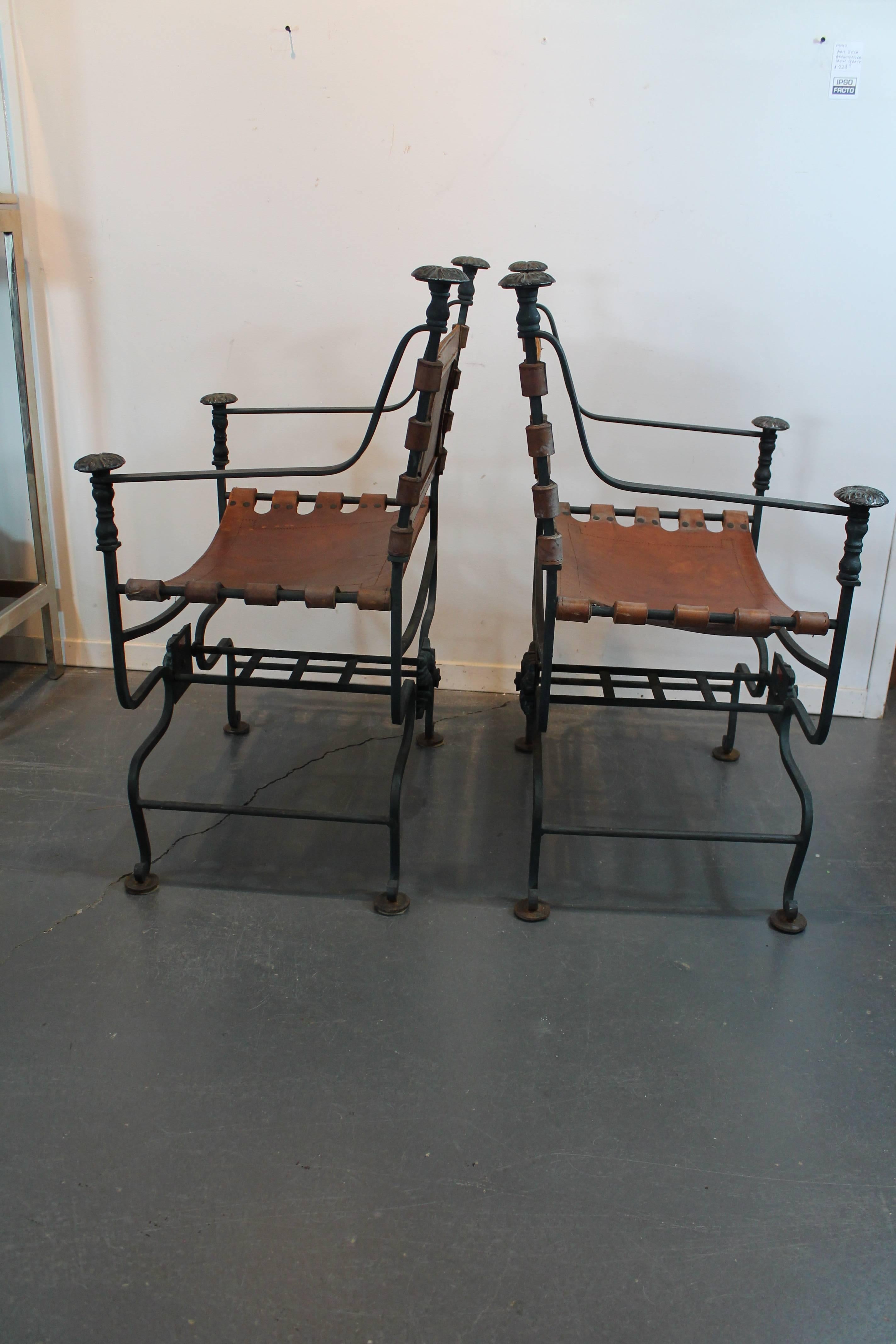 Strong graphic pair of mid-20th century iron and thick leather Savonarola chairs with great patina on the cast bronze medallions and finials.