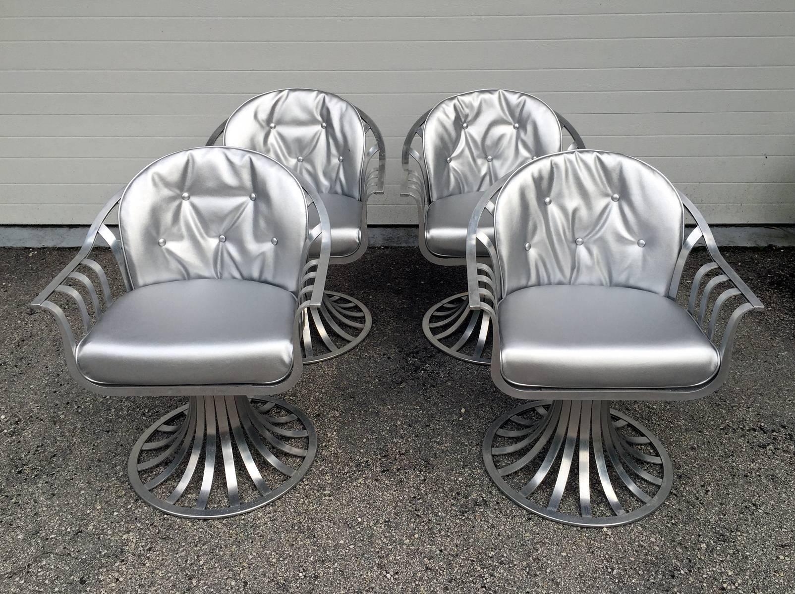 A great-looking set of four aluminum chairs by Russell Woodard. Sculptural form with curvy backrest continues into arms on swivel base. Stunning from all angels. New silver sterling upholstery add more glamour to the design. 
Very versatile chairs