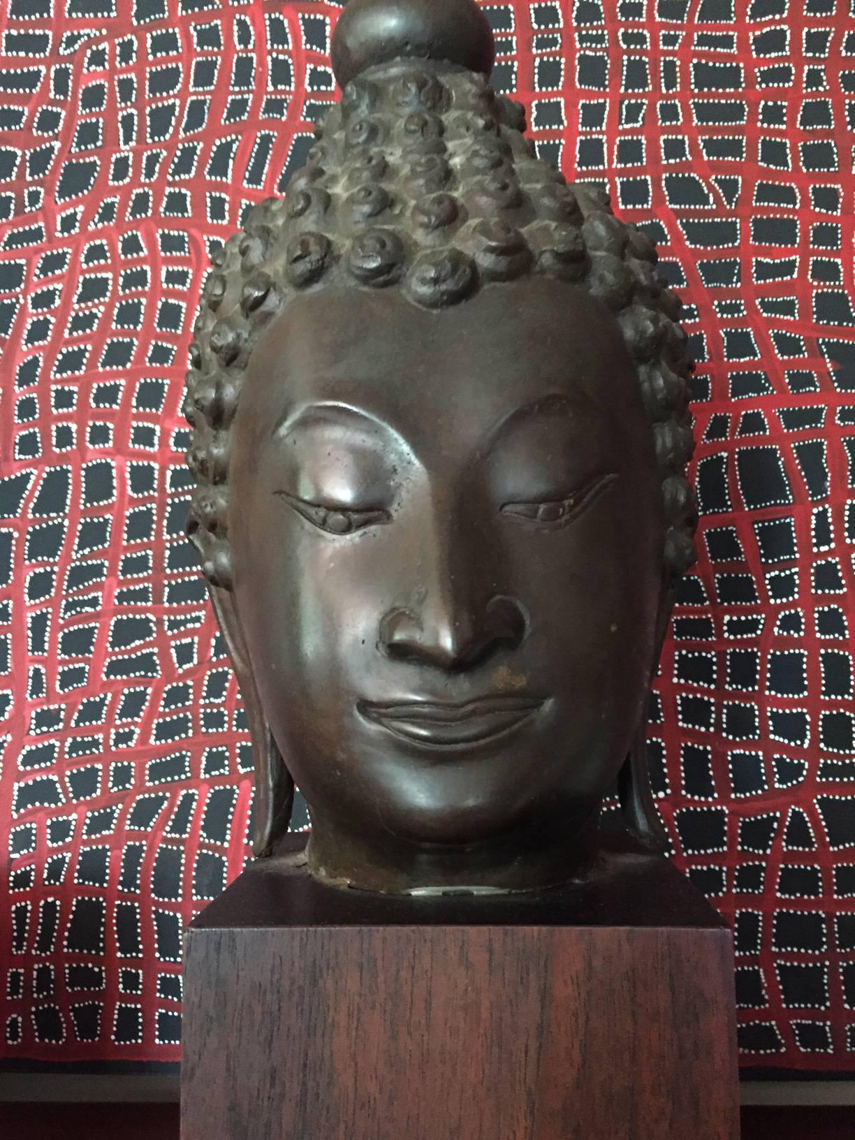 A cast bronze Buddha head fragment mounted on a wood base. Based on the typical facial expression and hair style, this Buddha head was likely from Lana Kingdom in Northern Thailand, likely late 19th century. Heavy patina throughout and chip on the