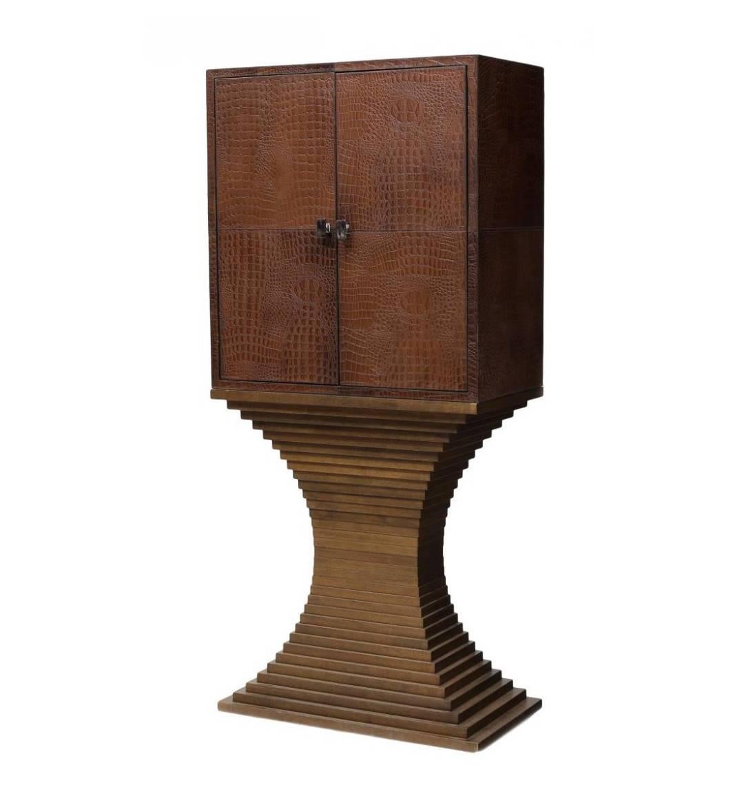 A very striking looking leather bar from England, circa 1970s. The bar with all glass interior is covered with embossed crocodile skin leather and supported by a sculpted tiered pedestal base. Two doors with chrome pulls open to a single shelves