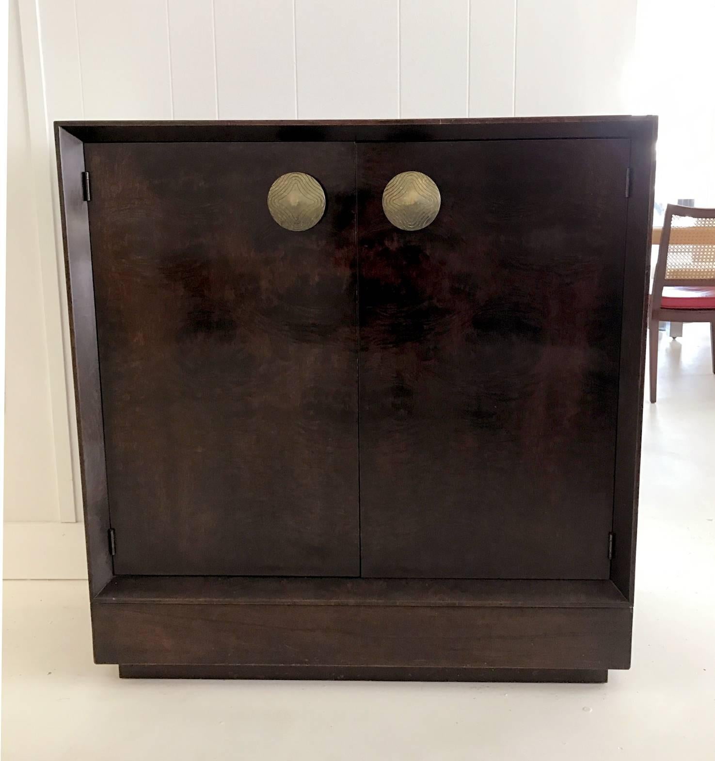 Art Deco cabinet/bookcase designed by Gilbert Rohde in 1940s and manufactured by Herman Miller. Exotic paldao veneer. It has two doors with large bronze gilt pulls and two interior shelves. Stenciled 4108 on the back.
