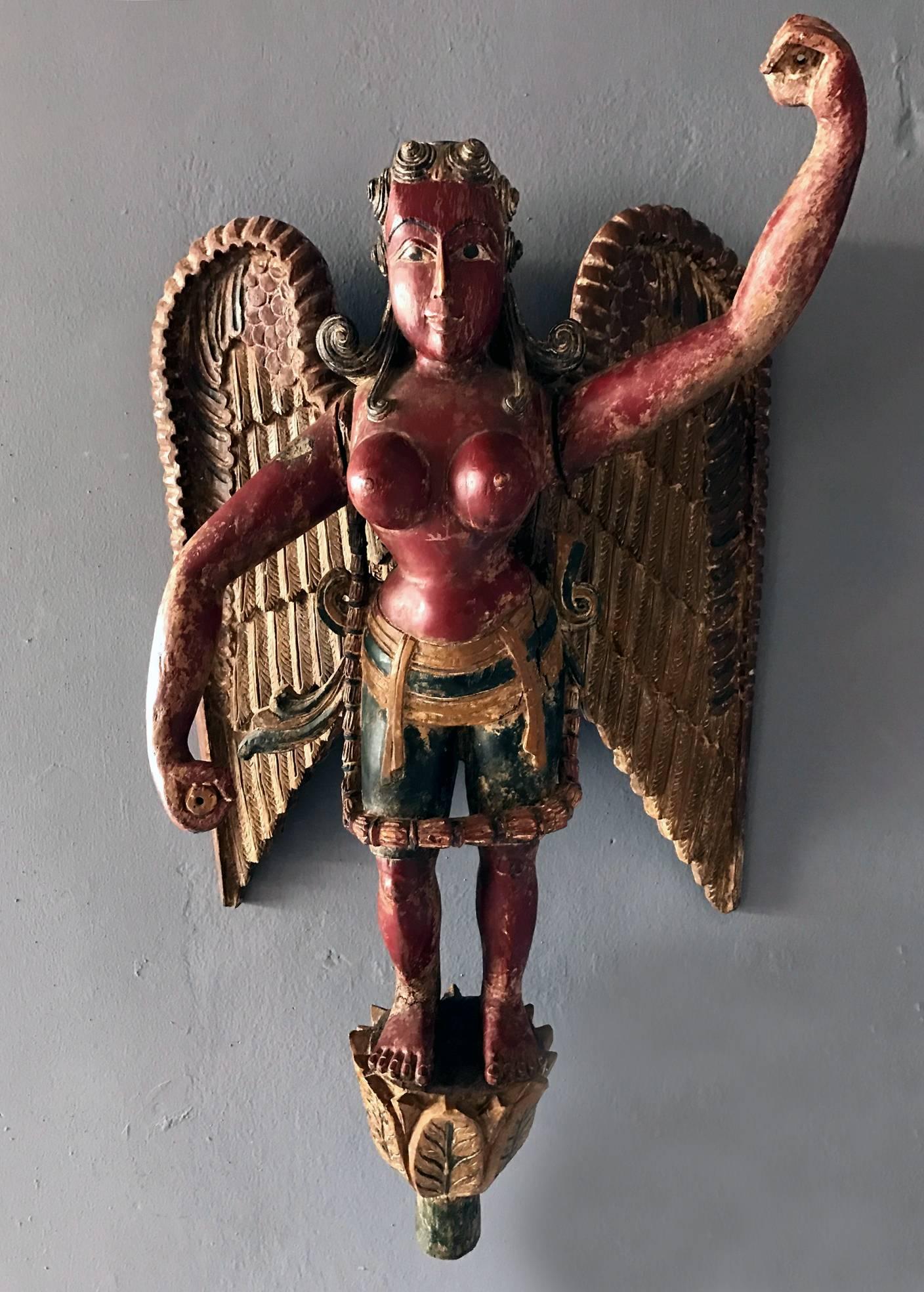 An interesting wood figure from India depicting a winged goddess, likely a female Garuda, circa 19th century. She stands on a lotus like pedestal and is dressed in a Dhoti like skirt with fully exposed breast. She has jointed arm and wings and her