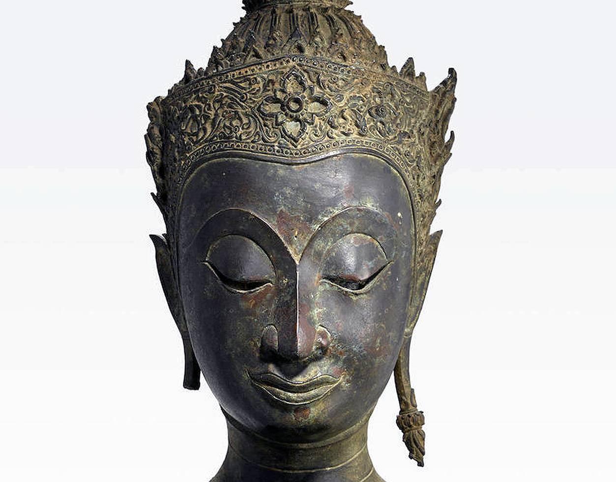 A Thai bronze Buddha head of Ayutthaya Period (1350 to 1767 A.D) on a fitted wood base. The style of this particular Buddha image is dated to the later Ayutthaya period circa 18th century, when it became common to depict Buddha with a lavish royal