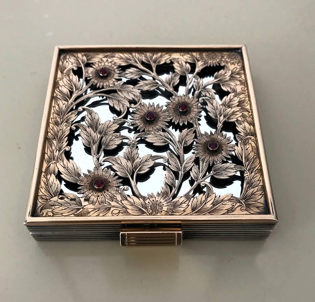 A stunning silver compact case or box by Boucheron Paris circa 1935, of Art Deco period and style. The case with ribbed surface was fitted with an elaborate pierced and engraved floral pattern gilt cover that is set with five cabochon rubies. 
The