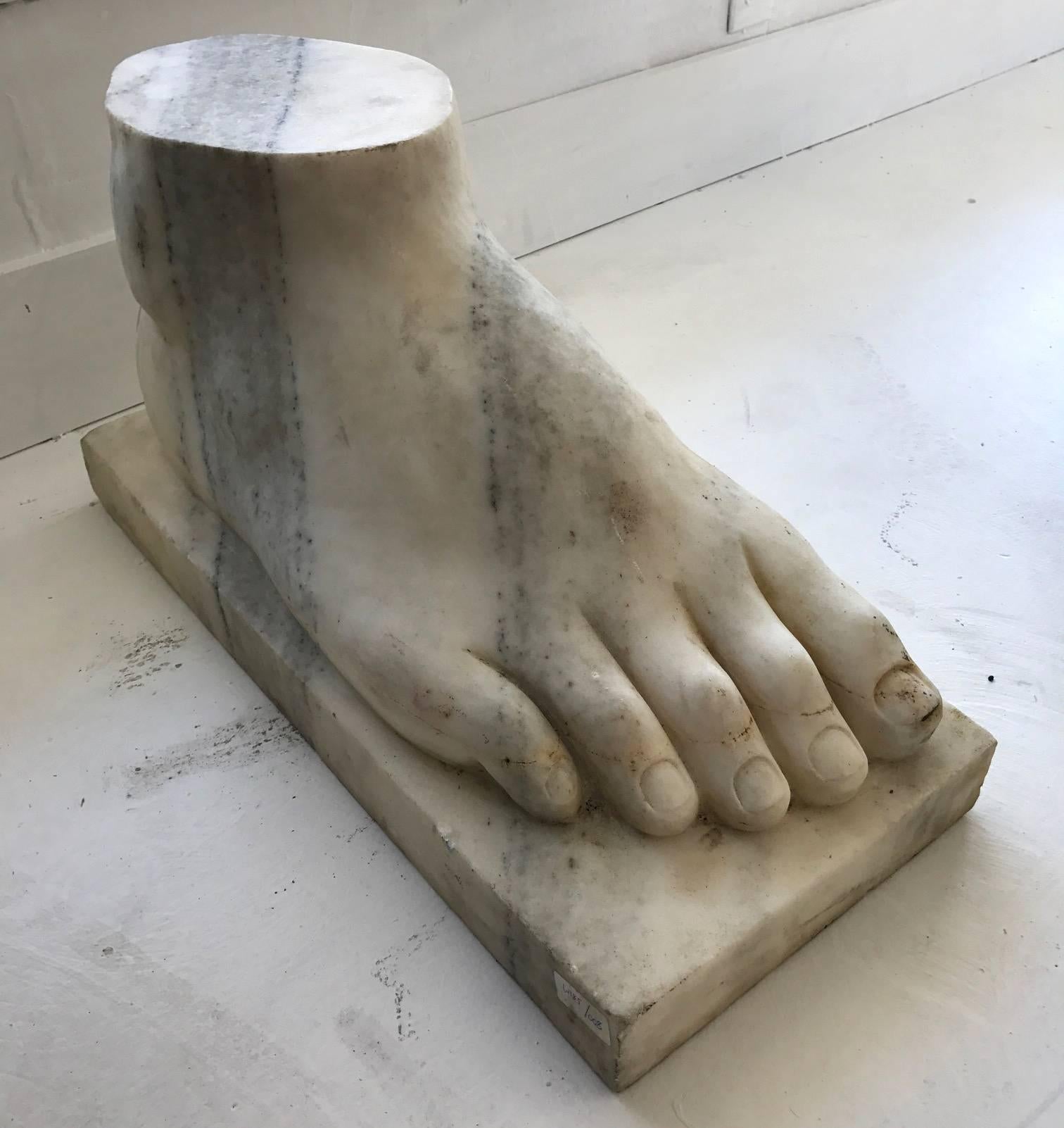 A craved marble foot on pedestal. Modeled after the Colossus of Rhodes. With nice detail and showing black veins, it piece can be used as a side table, a garden ornament or simply as a bespoken interior accessory. Solid marble and heavy.