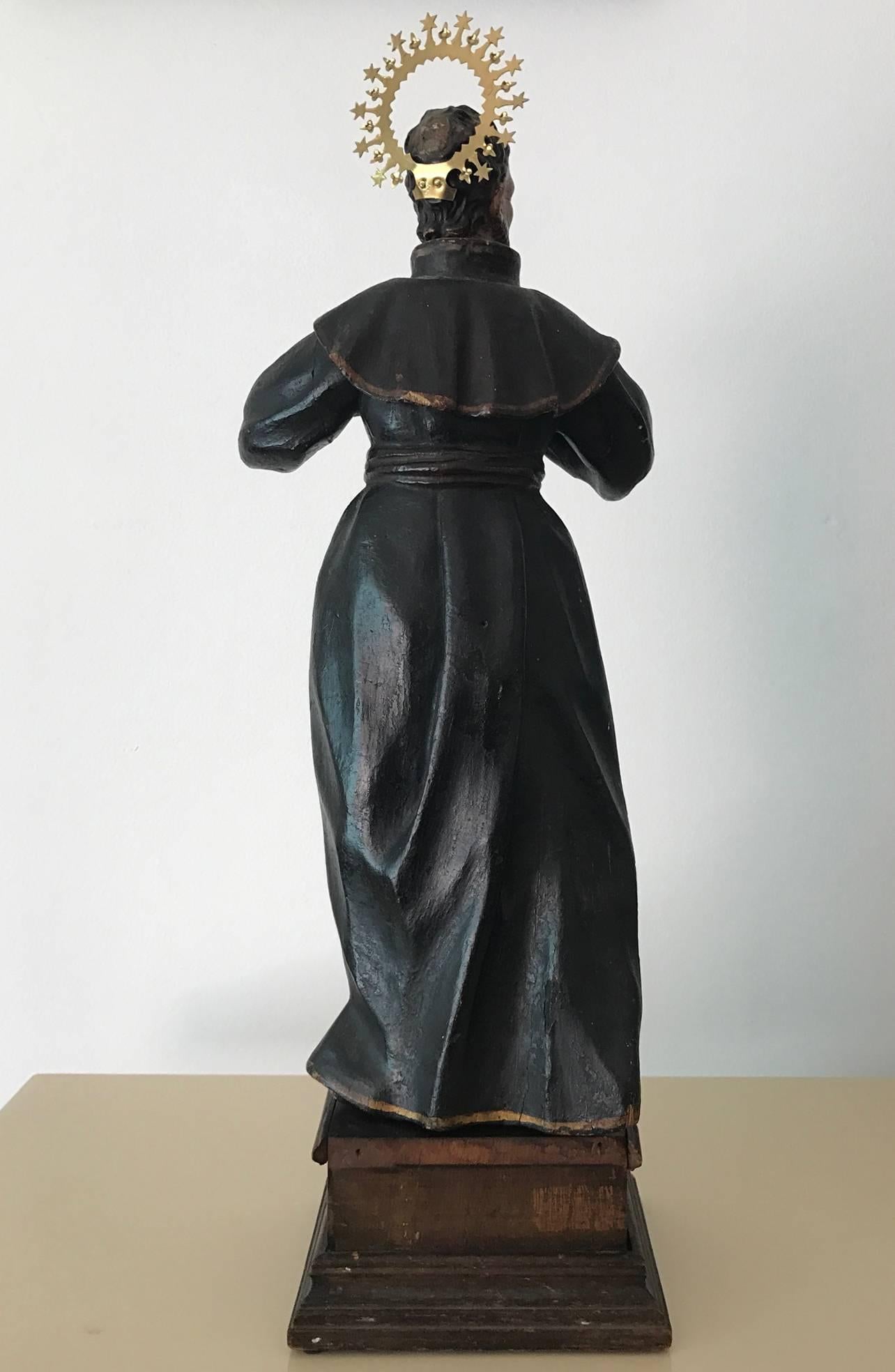 A well carved wood Santo from Spanish Colonial period circa 19th century, likely Mexico in origin. It depicts a saint in flowing black robe who rips it open to reveal its bare chest. sectional construction with head and hands carved separately in