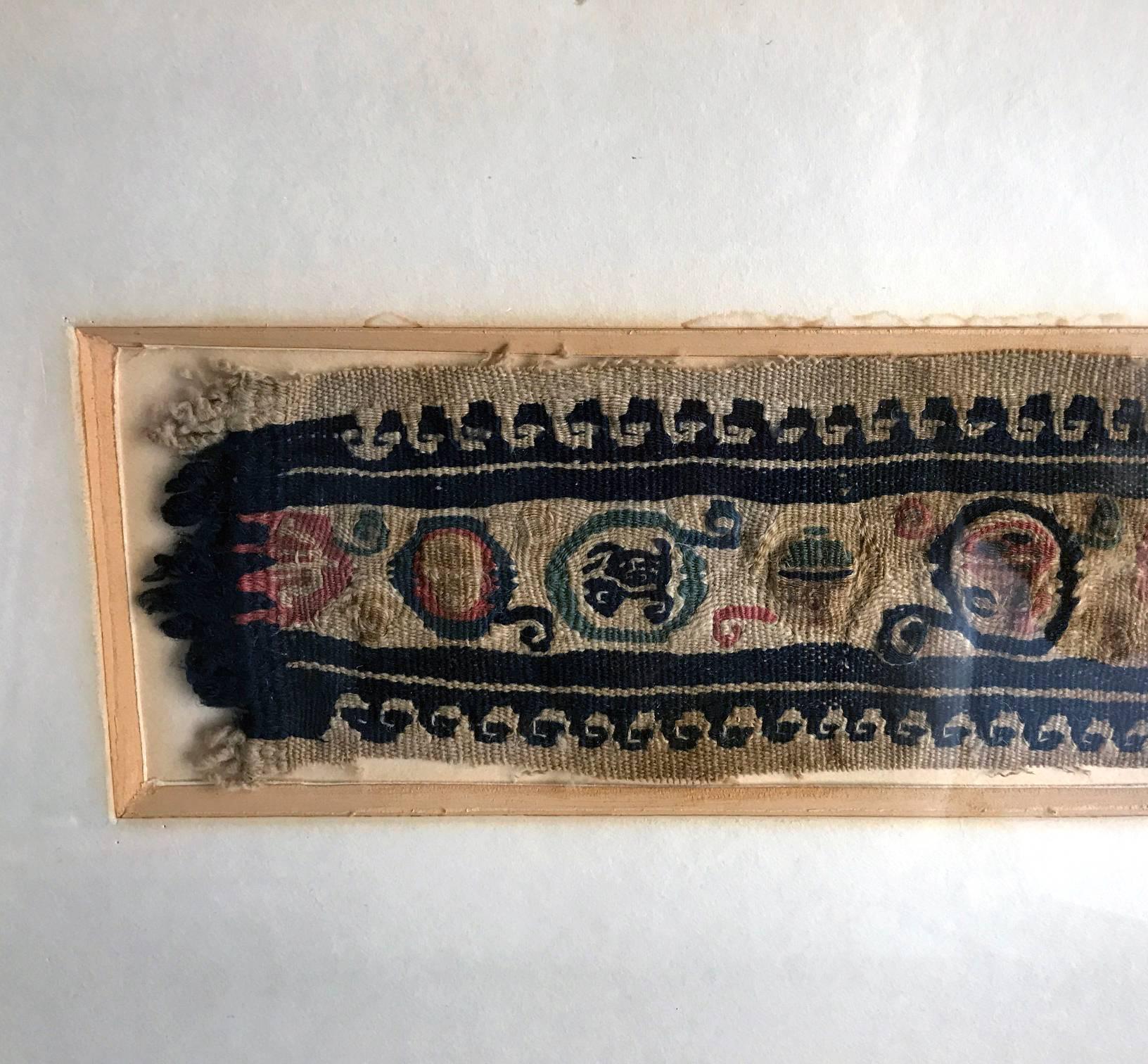 A small piece of antique coptic textile woven as a horizontal band with two linear Greek key borders flanking the central designs clustered in smaller abstract medallion forms, in the color of indigo with pink accent, this piece was likely from