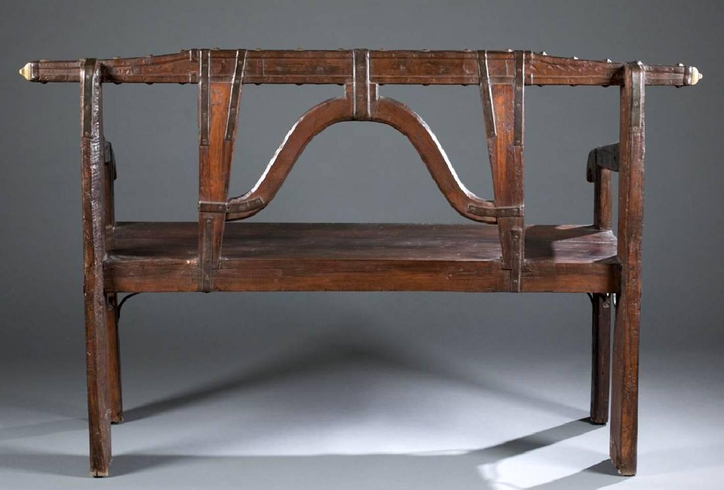 An antique Spanish Colonial bench likely from Peru, circa late 19th century. It displays a wonderful style that was clearly influenced by the indigenous aesthetic. The horse yoke shaped back is adorned with hammered and gilt metal insets, studs and