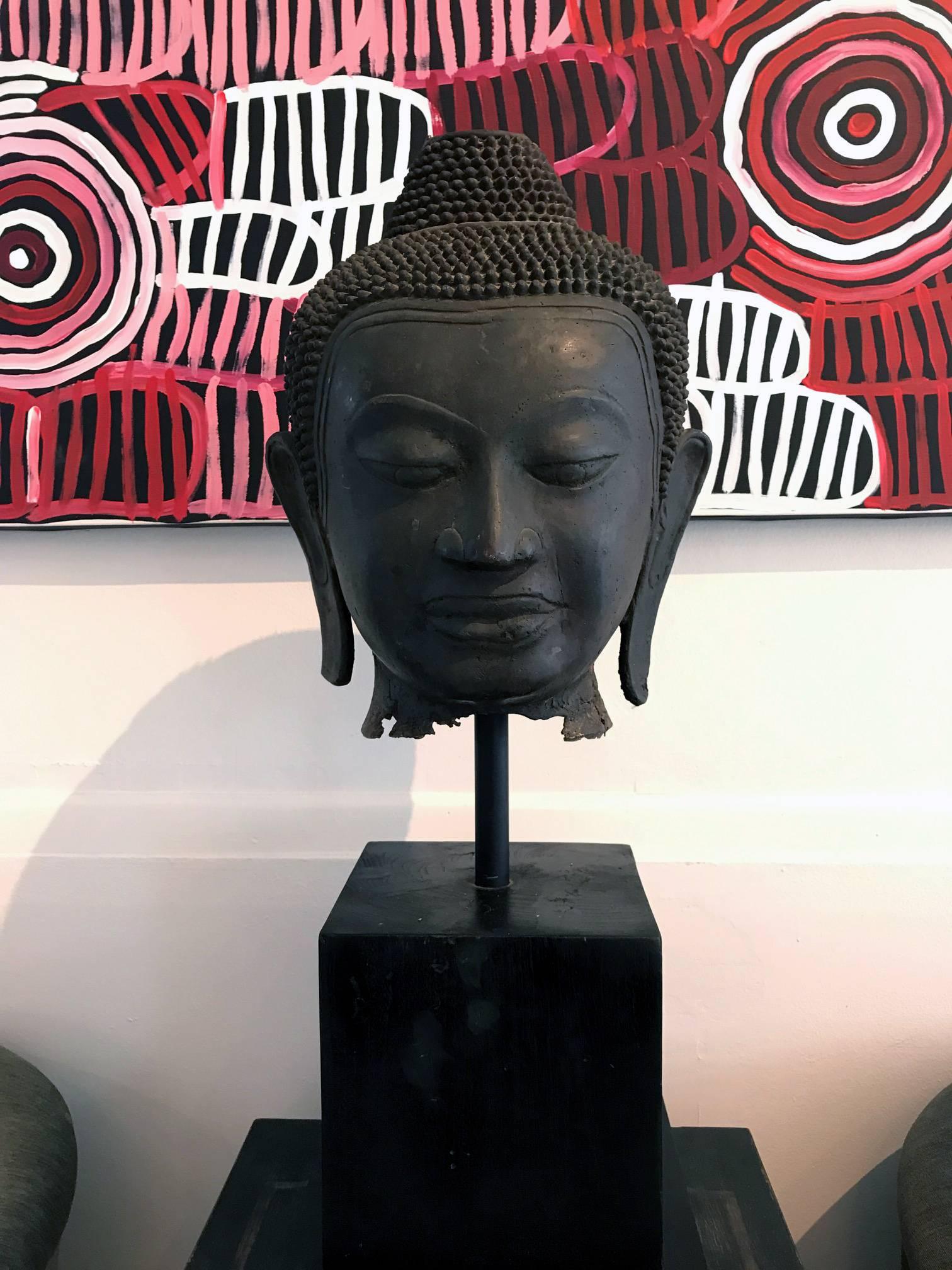 Un impressionnant fragment de tête de Bouddha en bronze présenté sur un support en bois vers la fin du 19e siècle. Le Bouddha a été coulé dans le style précoce 