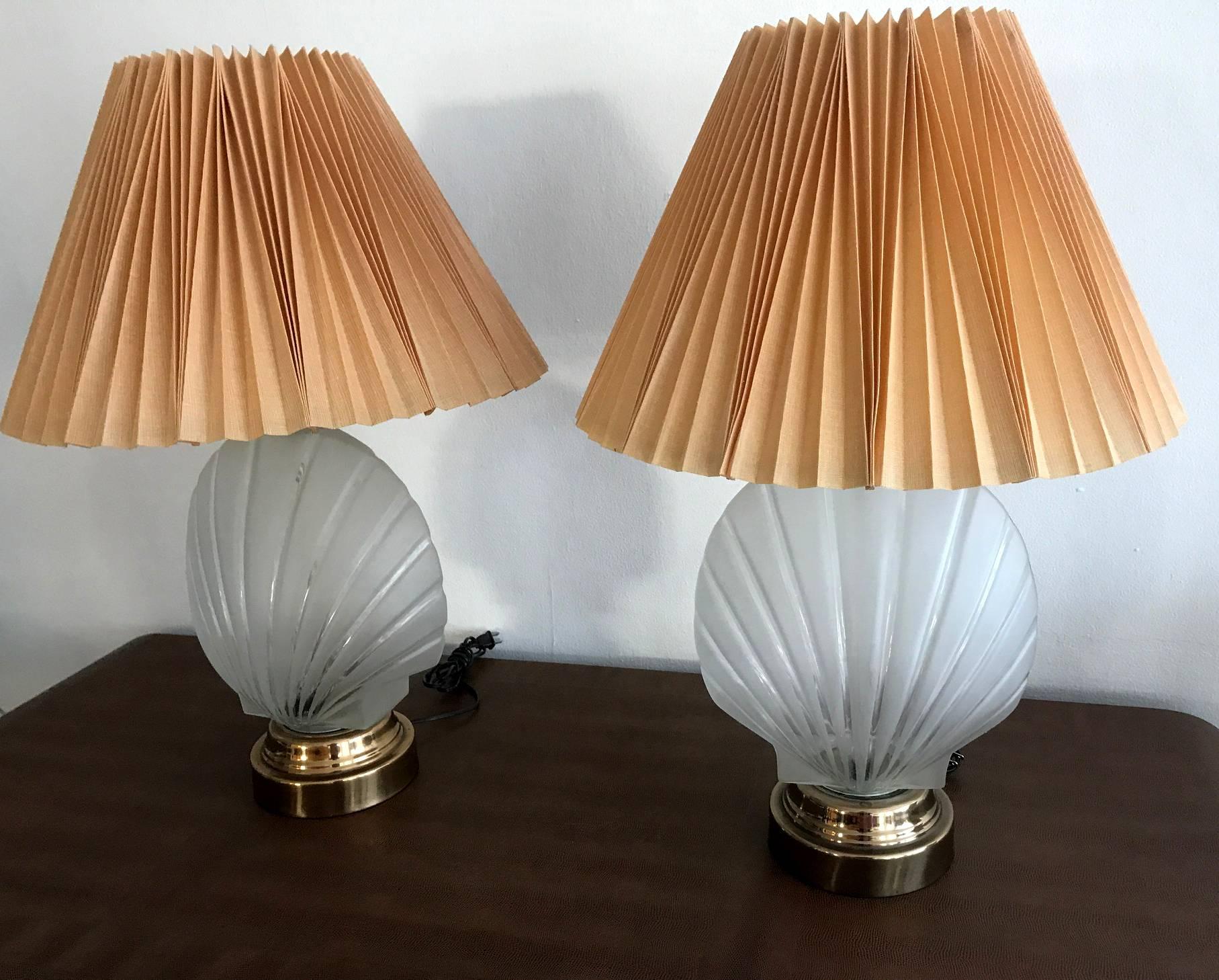 Very groovy and retro, this pair of table lamps features a frosted glass urn in a molded seashell form on polished brass base. The Classic ocean motif is given an spin in the Hollywood Regency fashion. The shades are very well designed in an