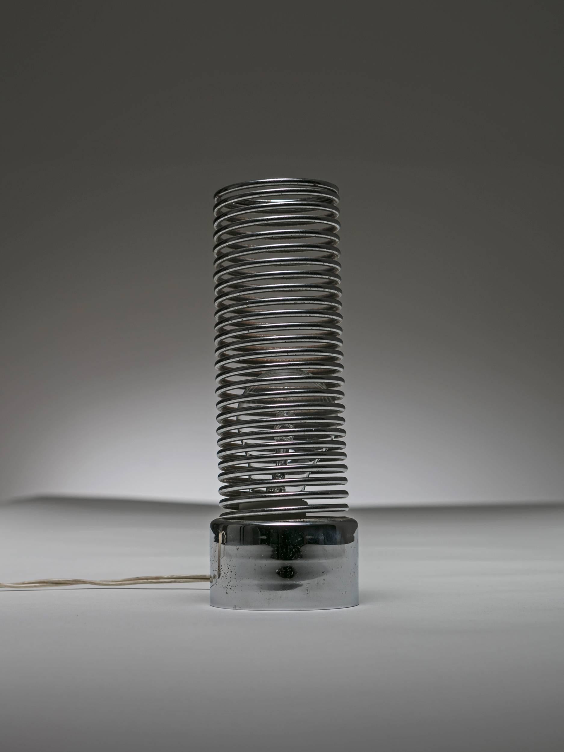 Lampe de table Spring par Harvey Guzzini.
Le socle en métal lourd accueille l'ampoule dont la lumière est diffusée en douceur le long du ressort métallique.
