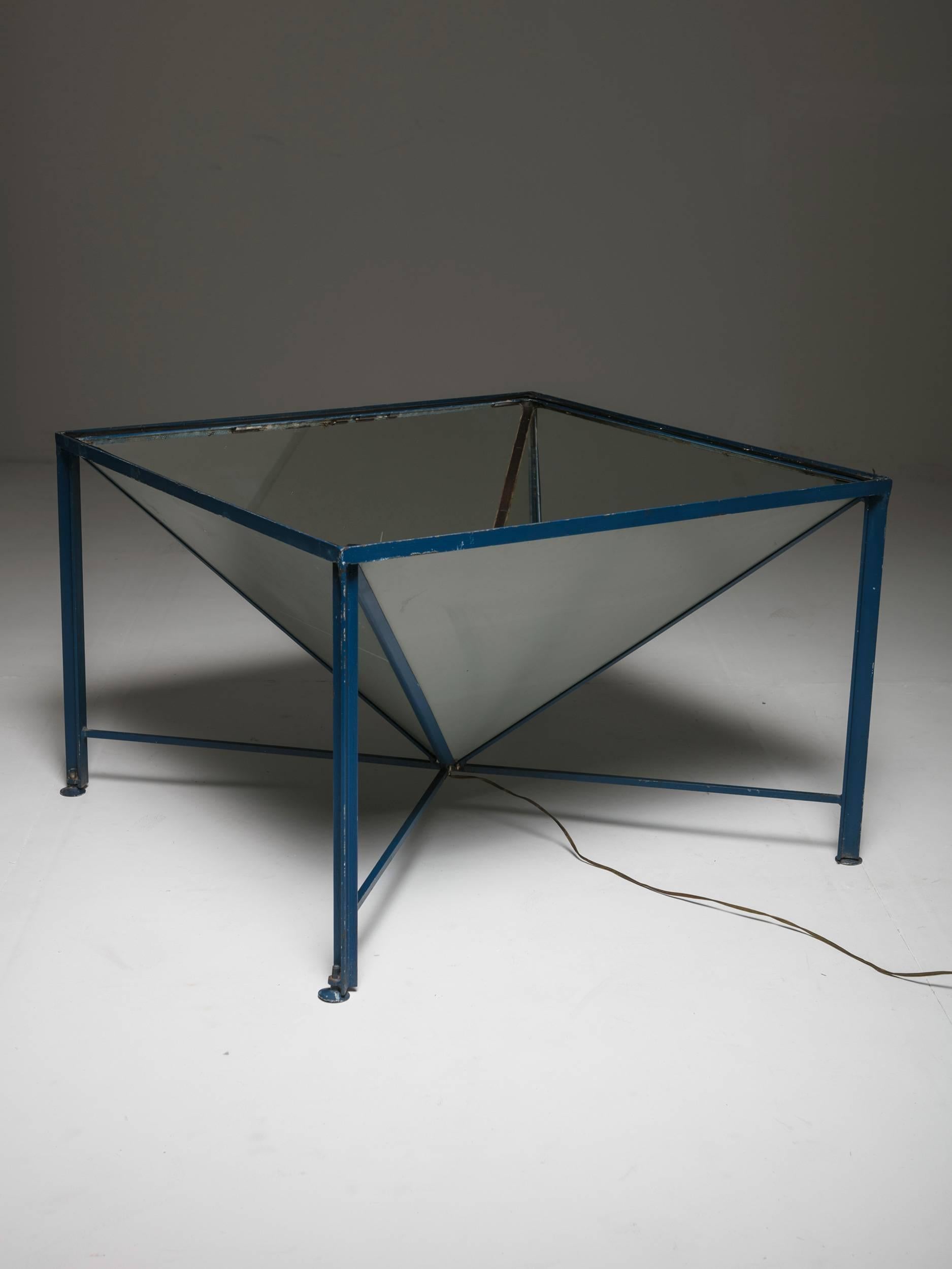 Table d'éclairage unique.
Un cadre en métal bleu émaillé supporte une pyramide de verre miroitée de bas en haut avec une lumière dans la partie inférieure. Pieds réglables et plateau en verre épais et transparent.
