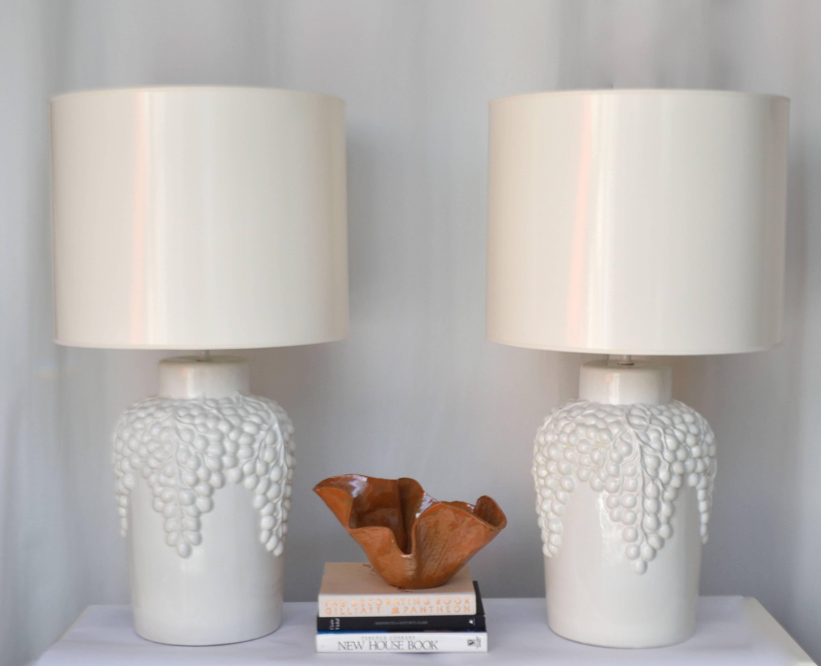Glamorous pair of Hollywood Regency Blanc de Chine jar form table lamps, Italy, circa 1950s-1960s. These striking artisan thrown lamps are finished in a white glaze and adorned with a decorative grape motif. Wired with brass fittings.
Shades not