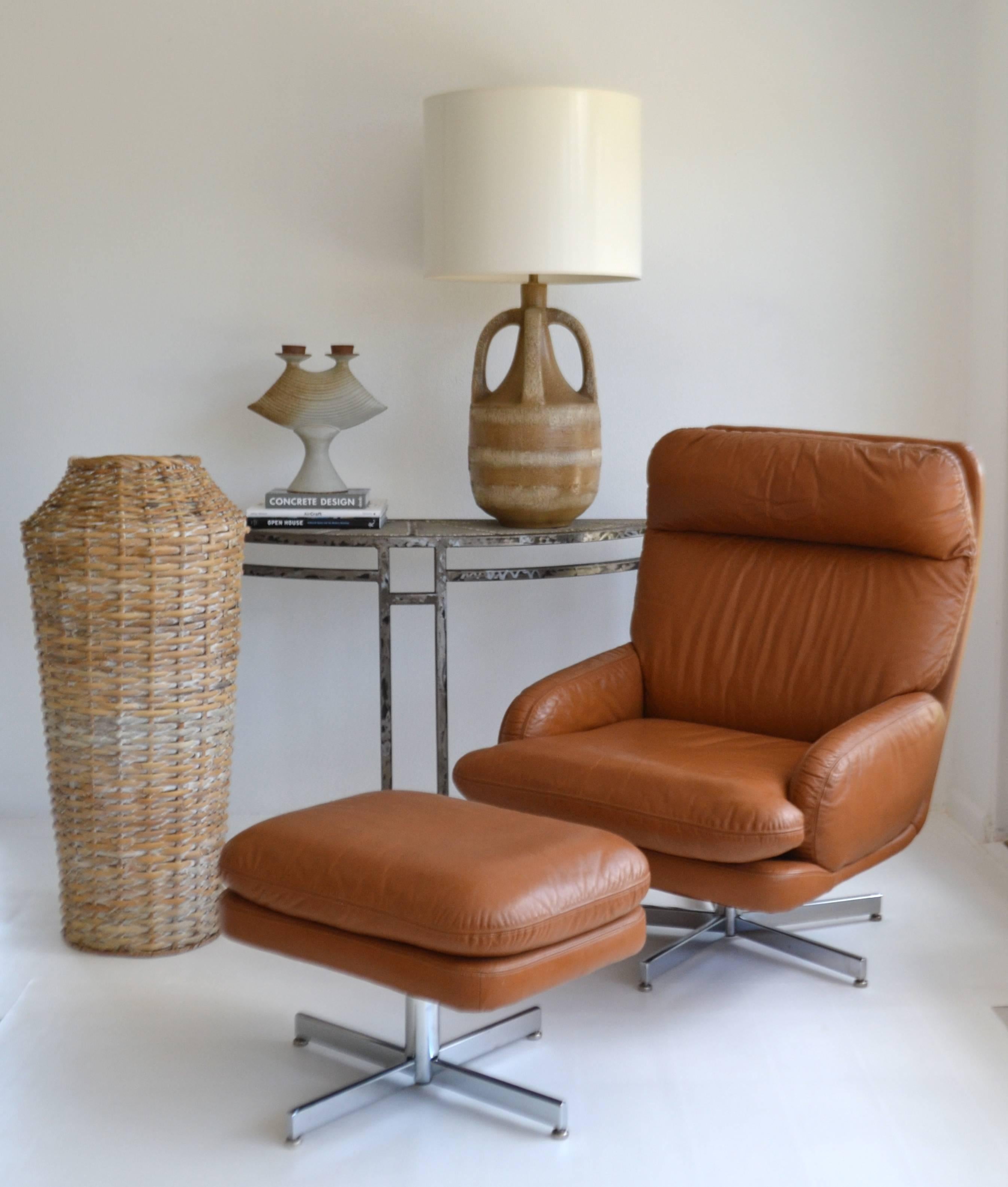Striking Mid-Century leather lounge chair and ottoman by Directional, circa 1960s - 1970s. This handsome club chair and accompanying stool are designed to swivel and are upholstered in the original brown leather upholstery with hand stitched