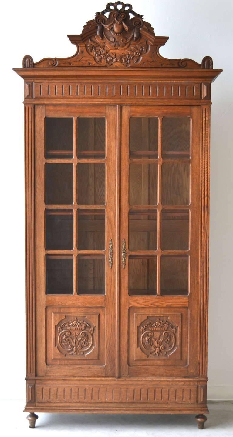 Exquisite French hand-carved oak bookcase / display cabinet, circa 19th century. This brilliant artisan carved cabinet with magnificent detail is accented with two glass front doors, brass decorative hardware, four adjustable shelves and has a