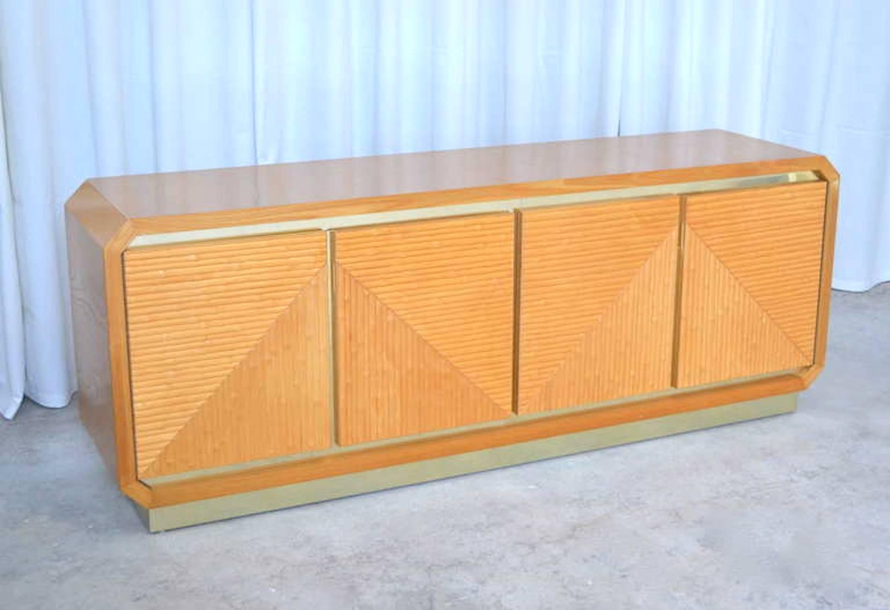 Striking Post-Modern faux bamboo sideboard with brass accents, circa 1970s. This handsome wood credenza consists of four doors decorated with faux carved bamboo geometric panels accentuated with brass details.  This highly decorative cabinet is
