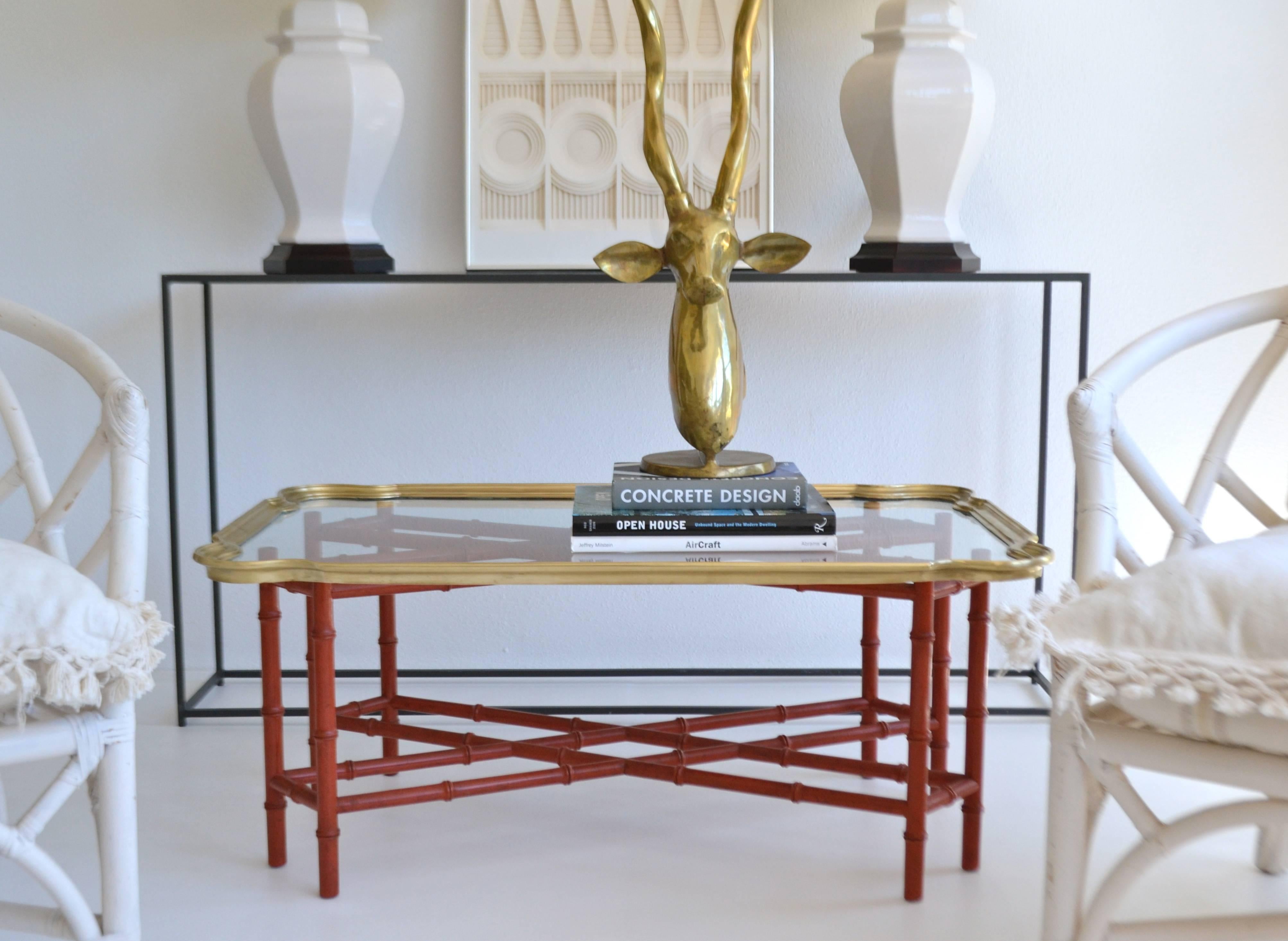 Striking Hollywood Regency faux bamboo tray top cocktail table, circa 1950s-1960s. This glamorous coffee table is designed with a polished brass and glass removable tray top mounted on a carved wooden red lacquered stretcher form base.