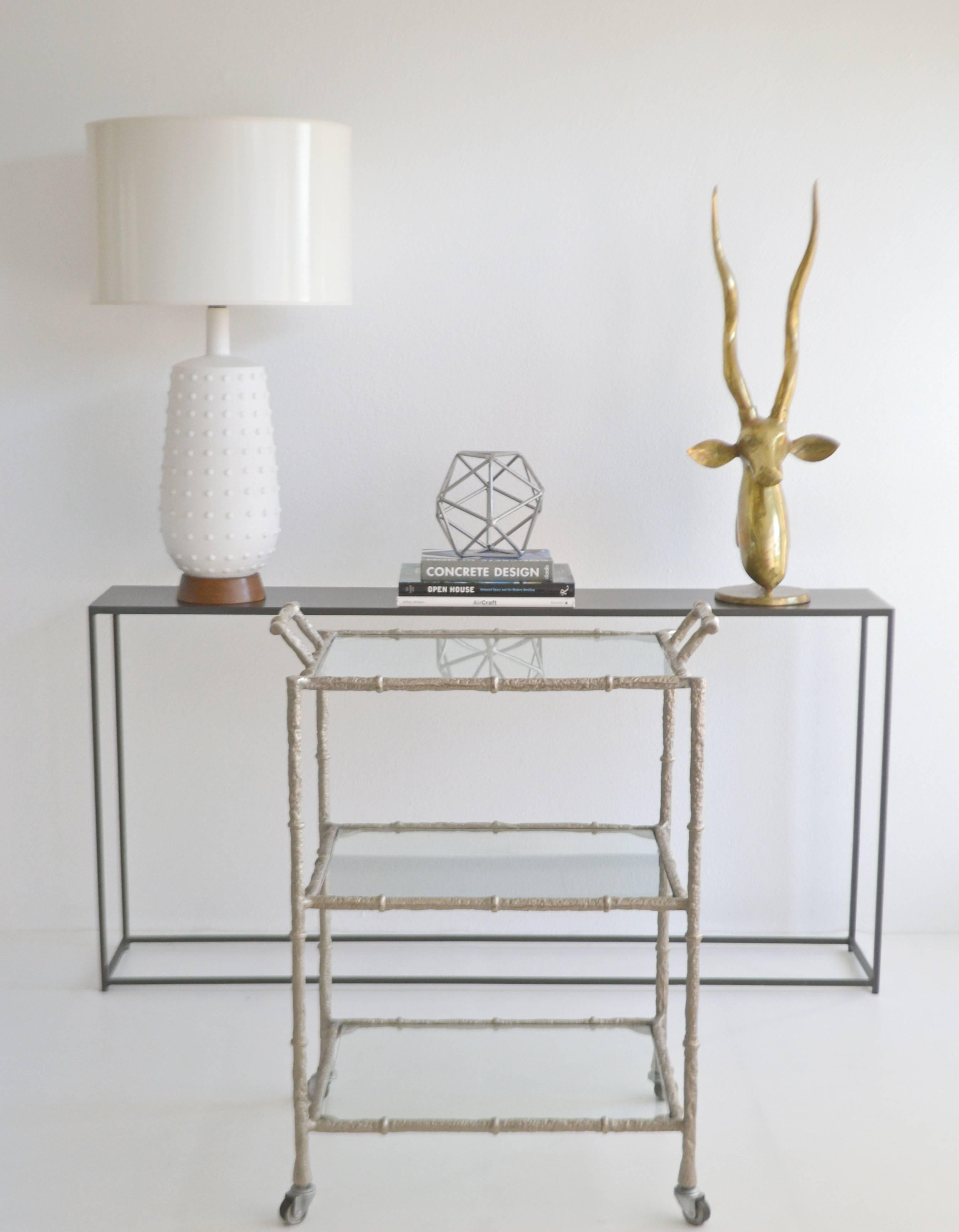 Glamorous Hollywood Regency faux bamboo nickel and glass bar cart, circa 1950s-1960s. This sculptural three-tiered artisan crafted drinks table or serving trolley is designed of etched hand-wrought burnished nickel and accented with glass inset