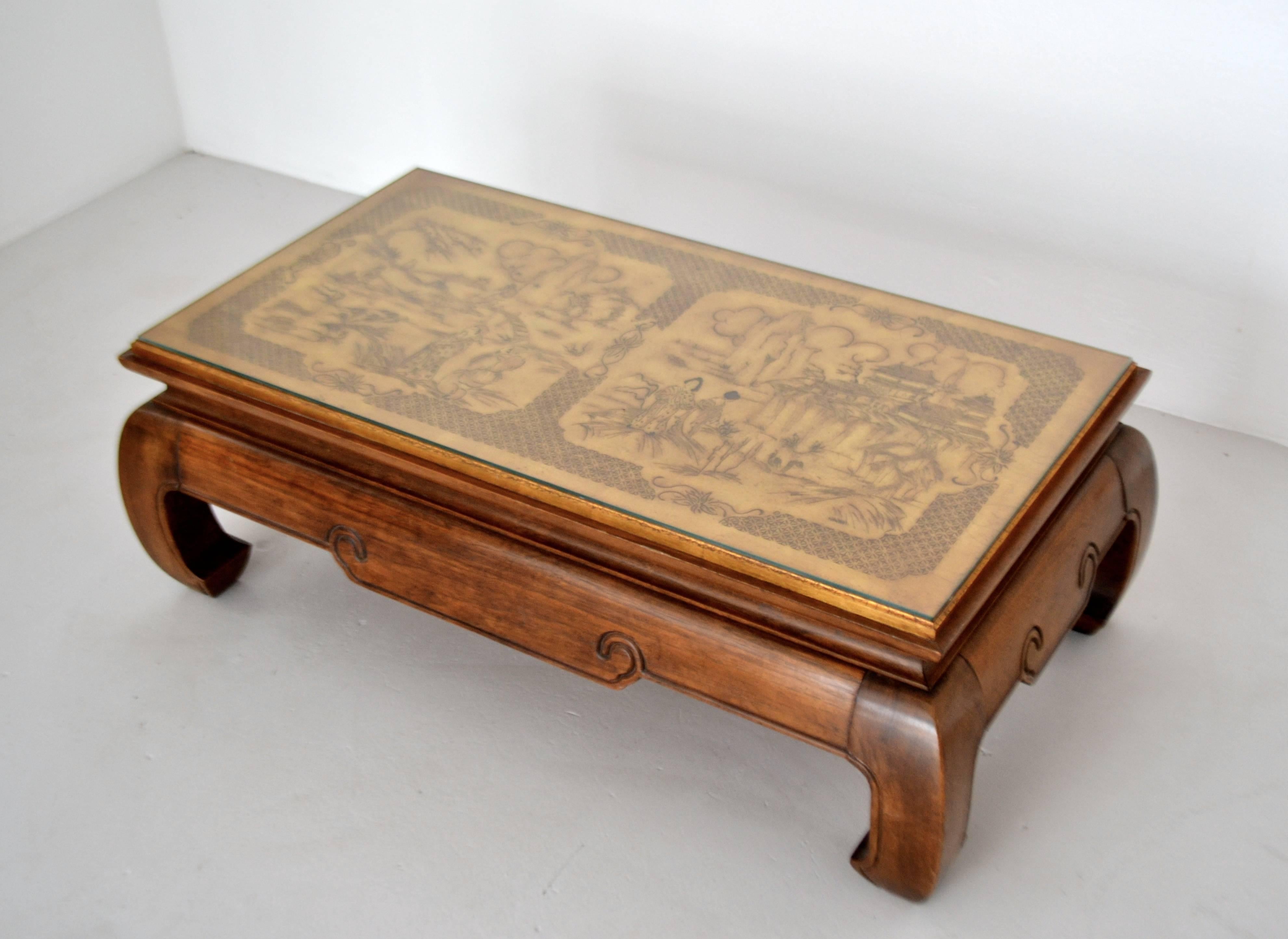 Stunning Hollywood Regency elmwood coffee table, circa 1950s. This striking artisan crafted hardwood cocktail table is designed with a gilt accented chinoiserie inspired hand etched wooden top.