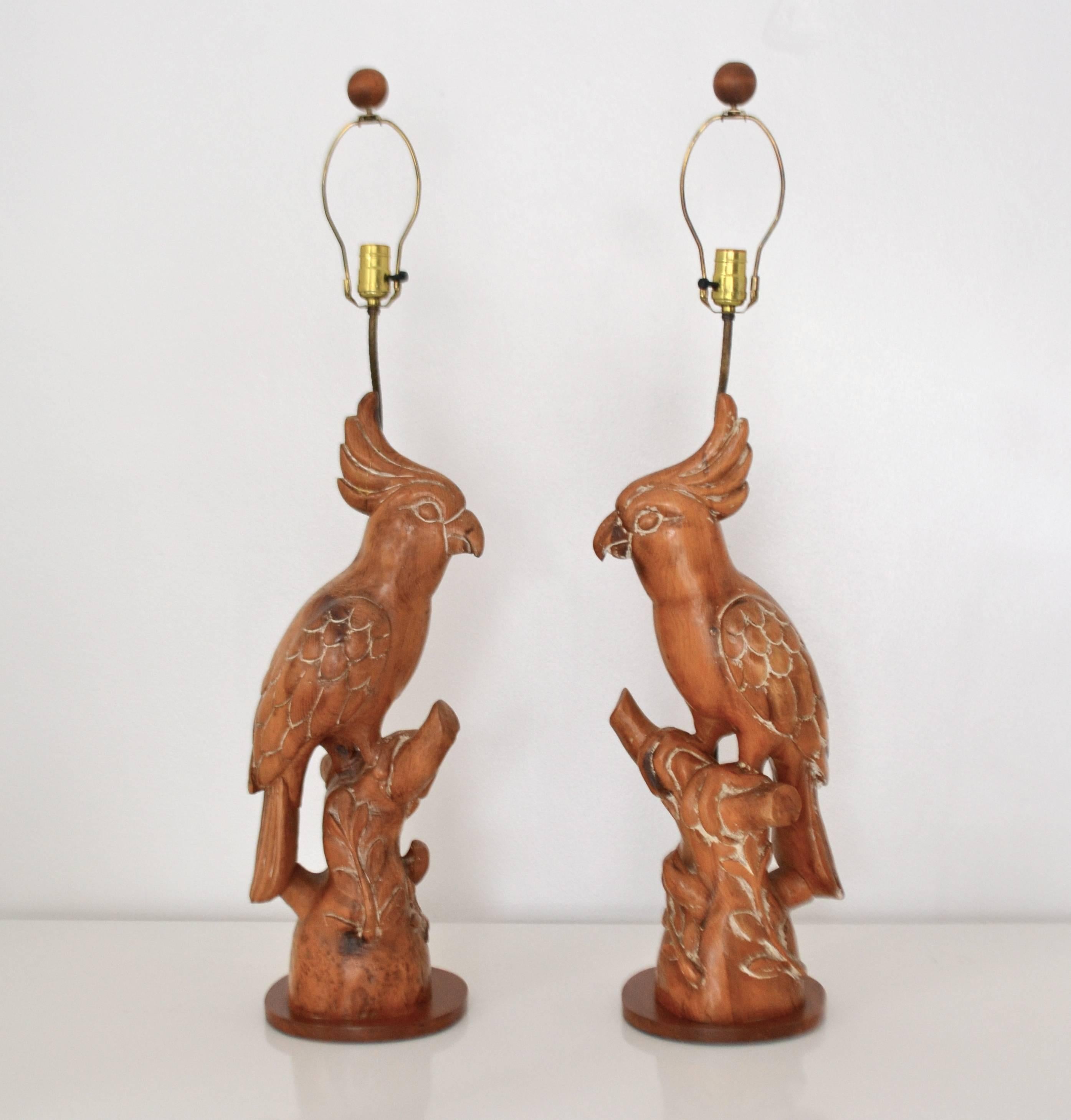 Striking pair of midcentury hand carved wooden parrot form table lamps, circa 1950s-1960s. These stunning artisan crafted sculptural lamps are wired with brass fittings. Shades not included.

Measurements: The overall height is 43